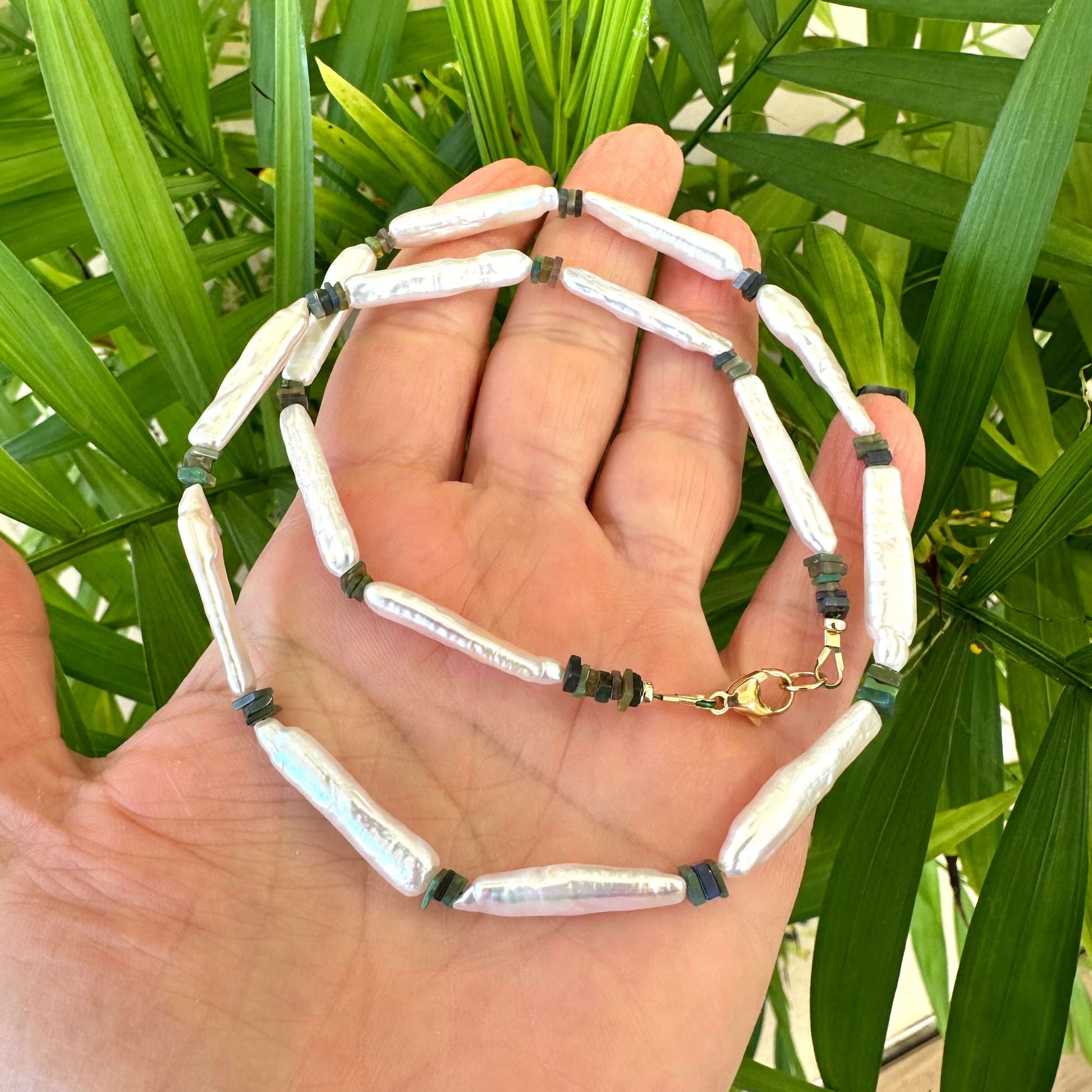 Close-up of biwa pearl and black opal necklace in hand, natural light setting