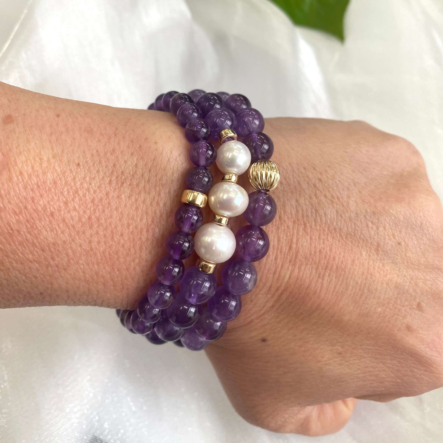 Two amethyst bracelets worn with an amethyst and pearl bracelet on wrist