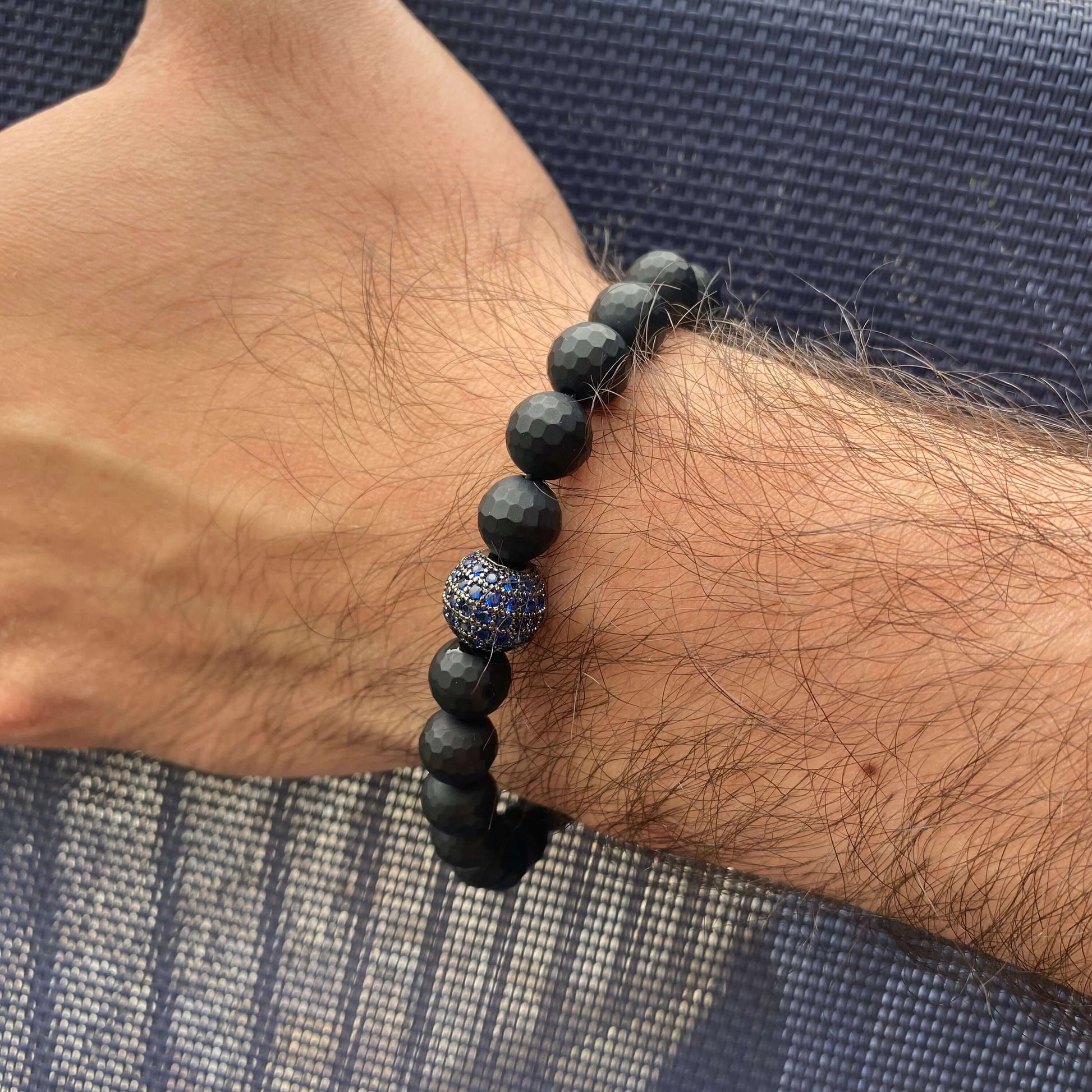 Matte black onyx mens bracelet on a wrist, featuring 8mm faceted beads and a blue CZ centerpiece.