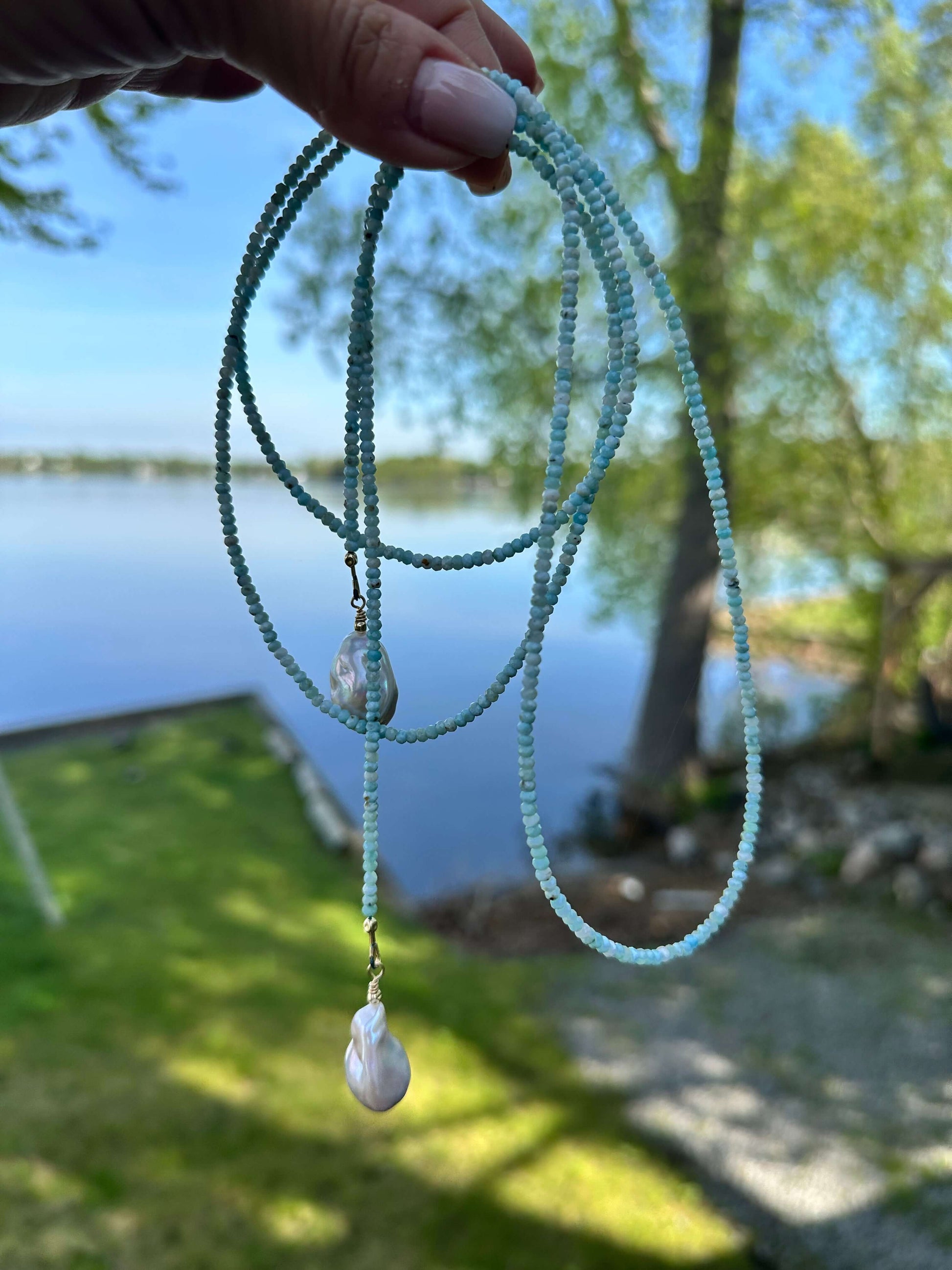 Blue Larimar Lariat Necklace held against lake and grass background — natural gemstone and pearl necklace handcrafted by Loulia Pearl Jewelry