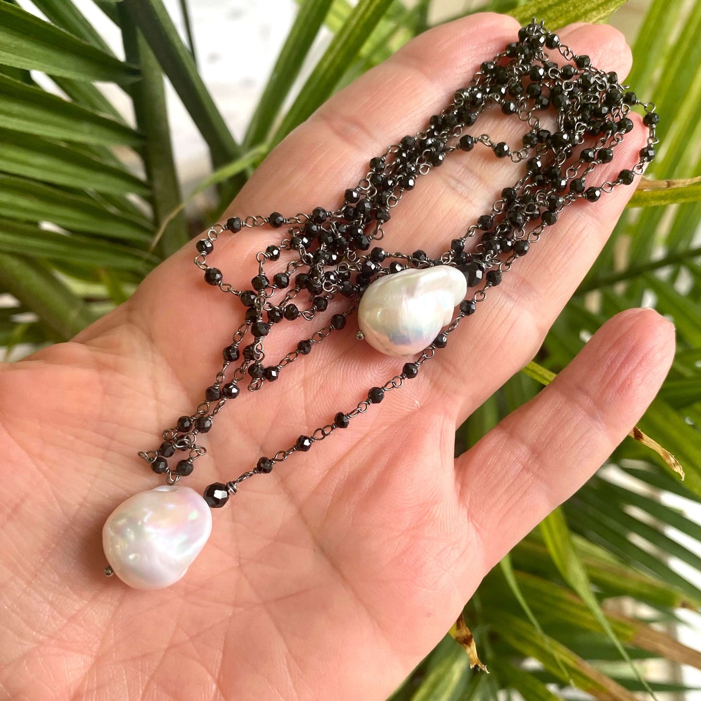 Black spinel lariat necklace held in hand against green foliage background showing natural shine
