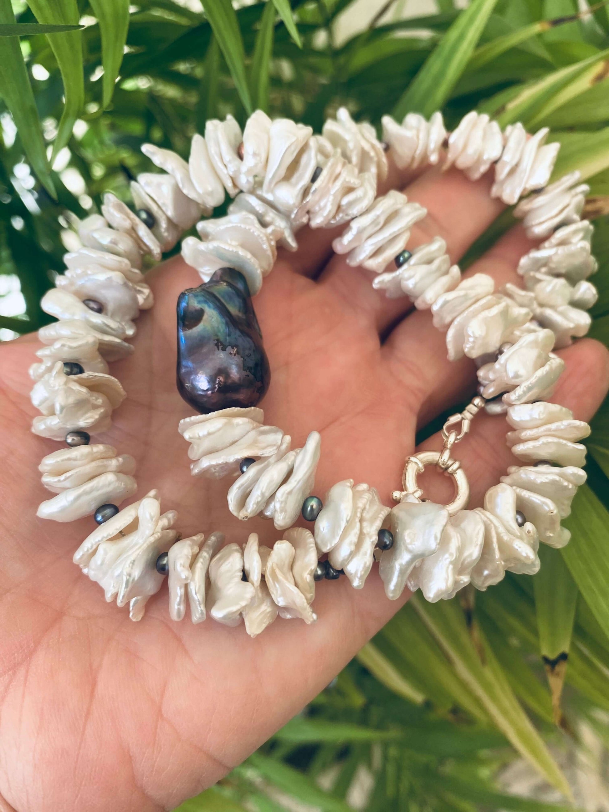 white cornflake pearl necklace with black baroque pearl pendant on a hand, showcasing organic beauty and unique sophistication.