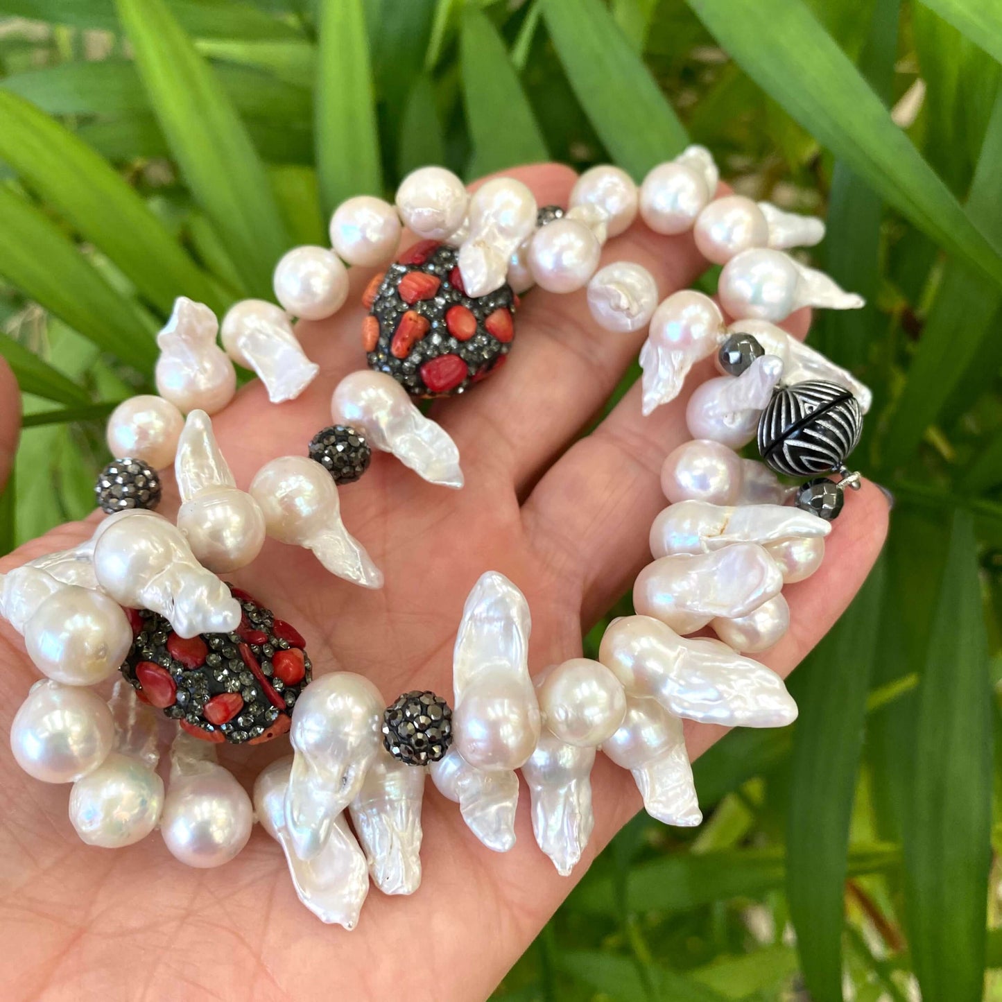 Baroque pearl jellyfish necklace red coral held in hand against green foliage handmade in Canada