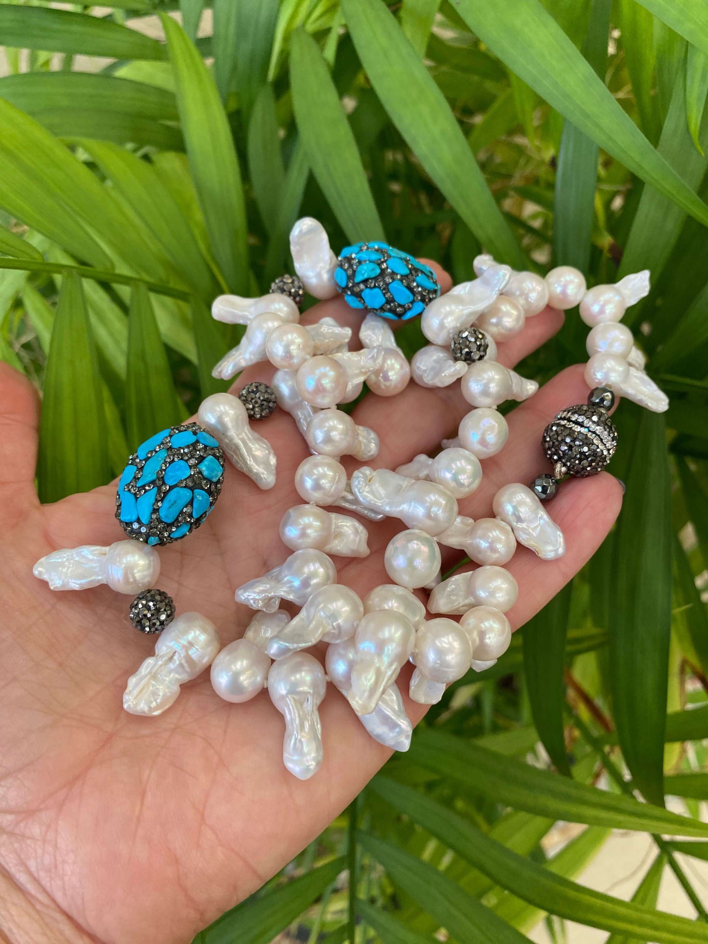 Baroque pearl jellyfish necklace held in hand against green leaf backdrop handmade in Canada