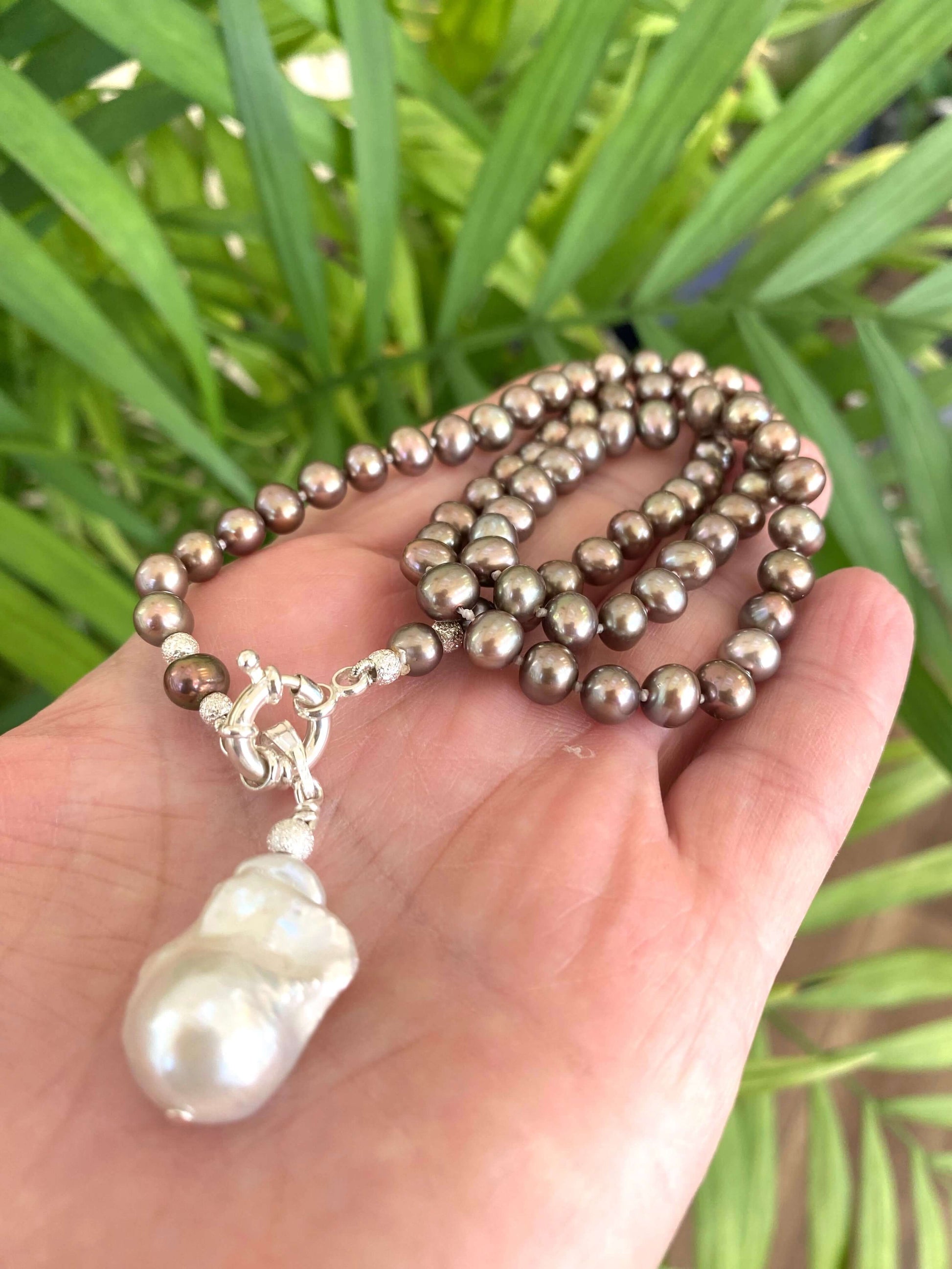 Bronze pearl necklace with white baroque pendant held in hand outdoors, showing natural sheen and warm metallic tones.