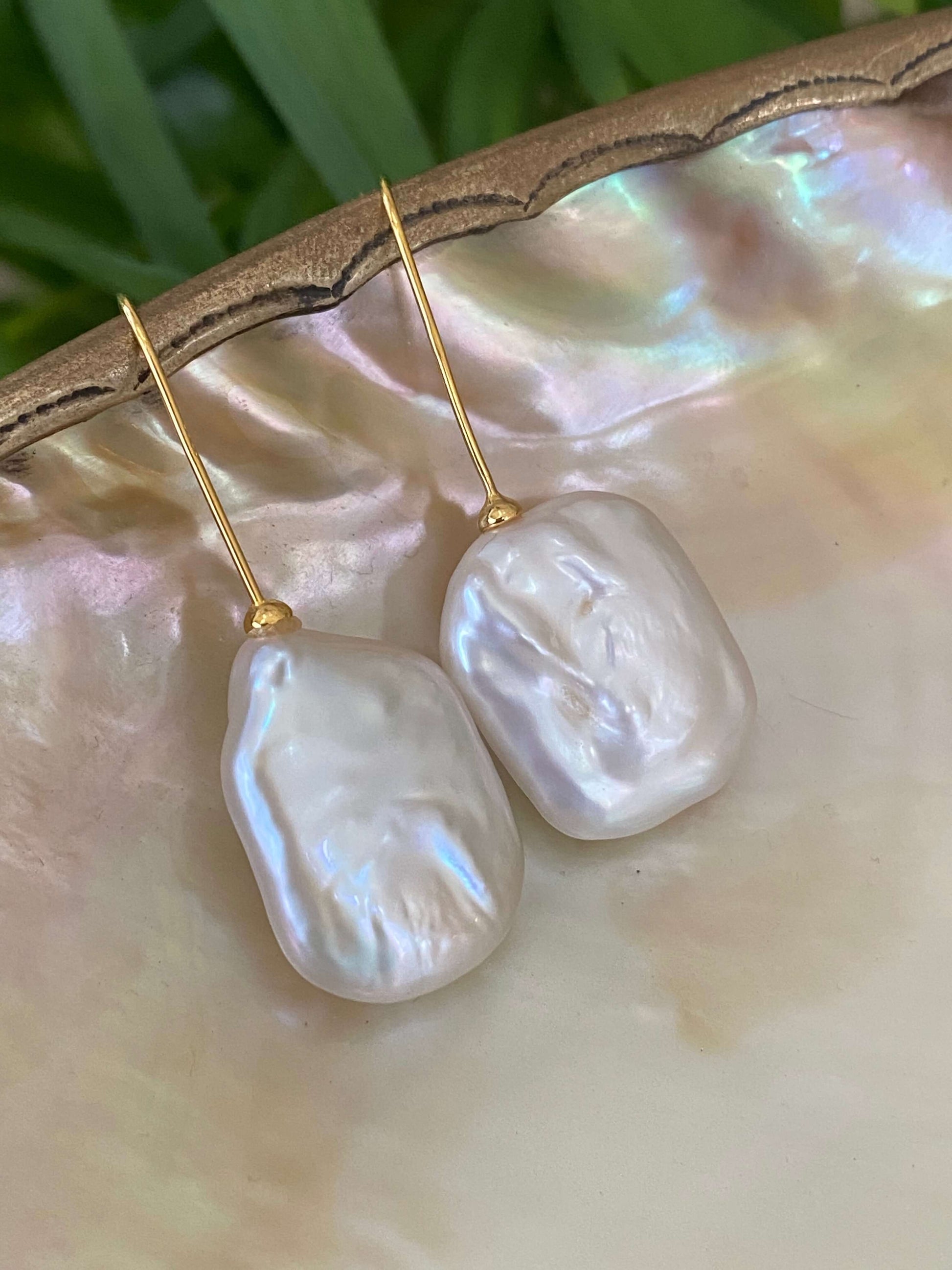 White freshwater pearl drop earrings in gold vermeil displayed on white pearl shell with green leaf background, designed and handmade in Canada.
