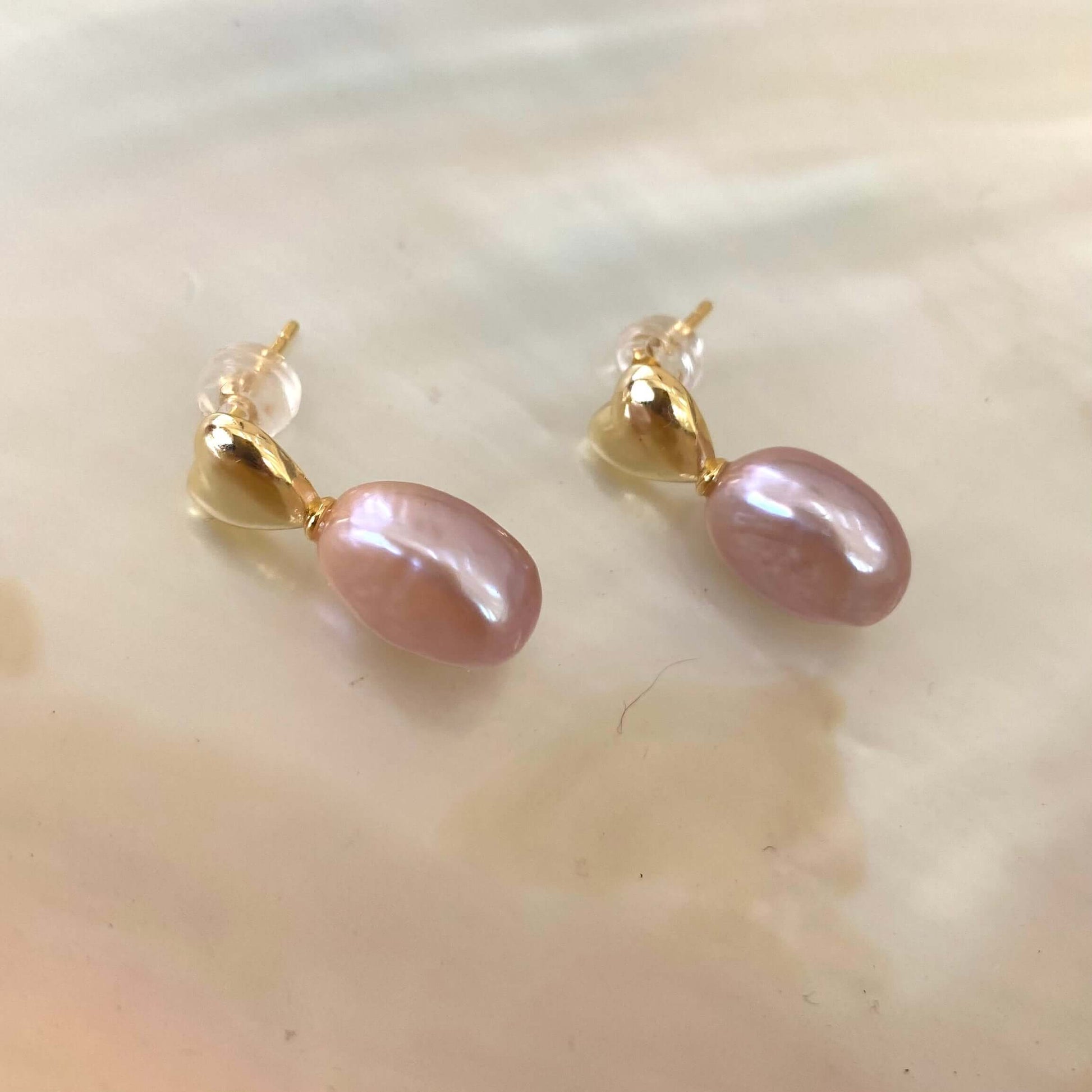 Heart Pearl Earrings – gold version close-up against white pearl shell