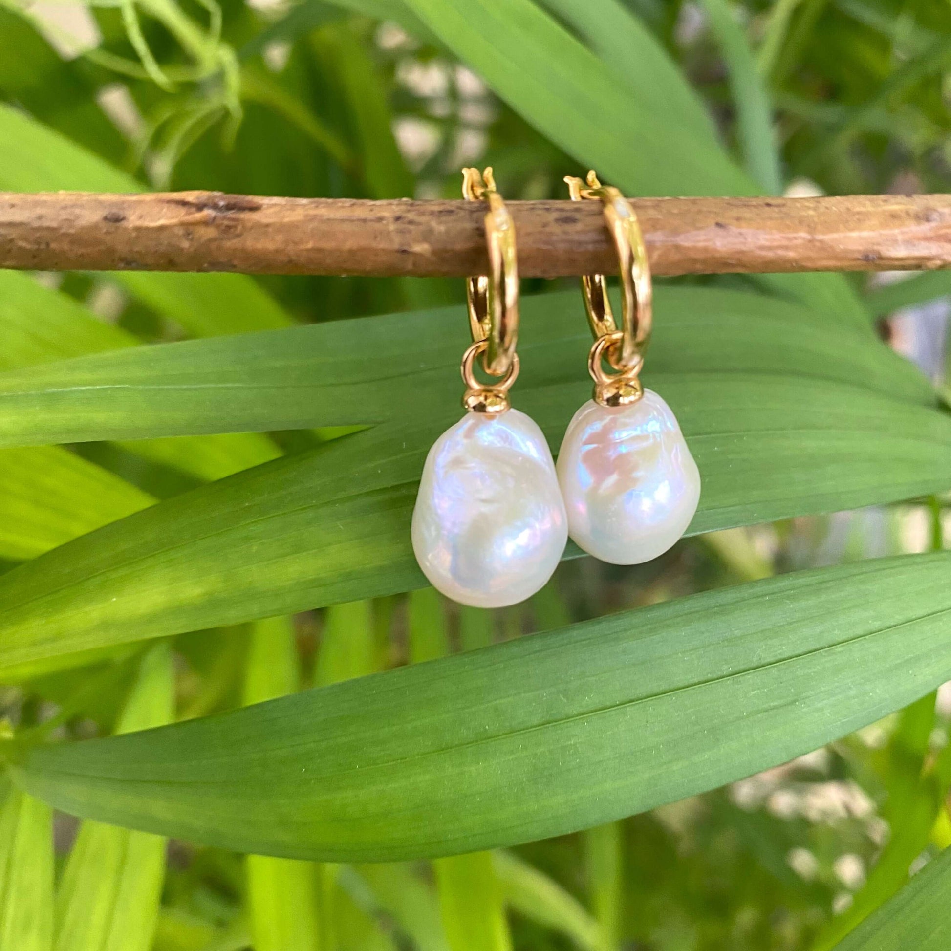 White Baroque Pearl Earrings – close-up against green leaf background