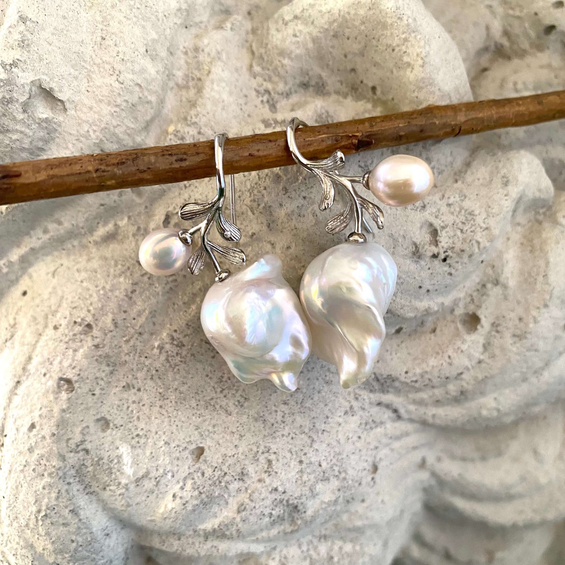 Close-up of baroque pearl earrings in silver with rose leaf design on white background