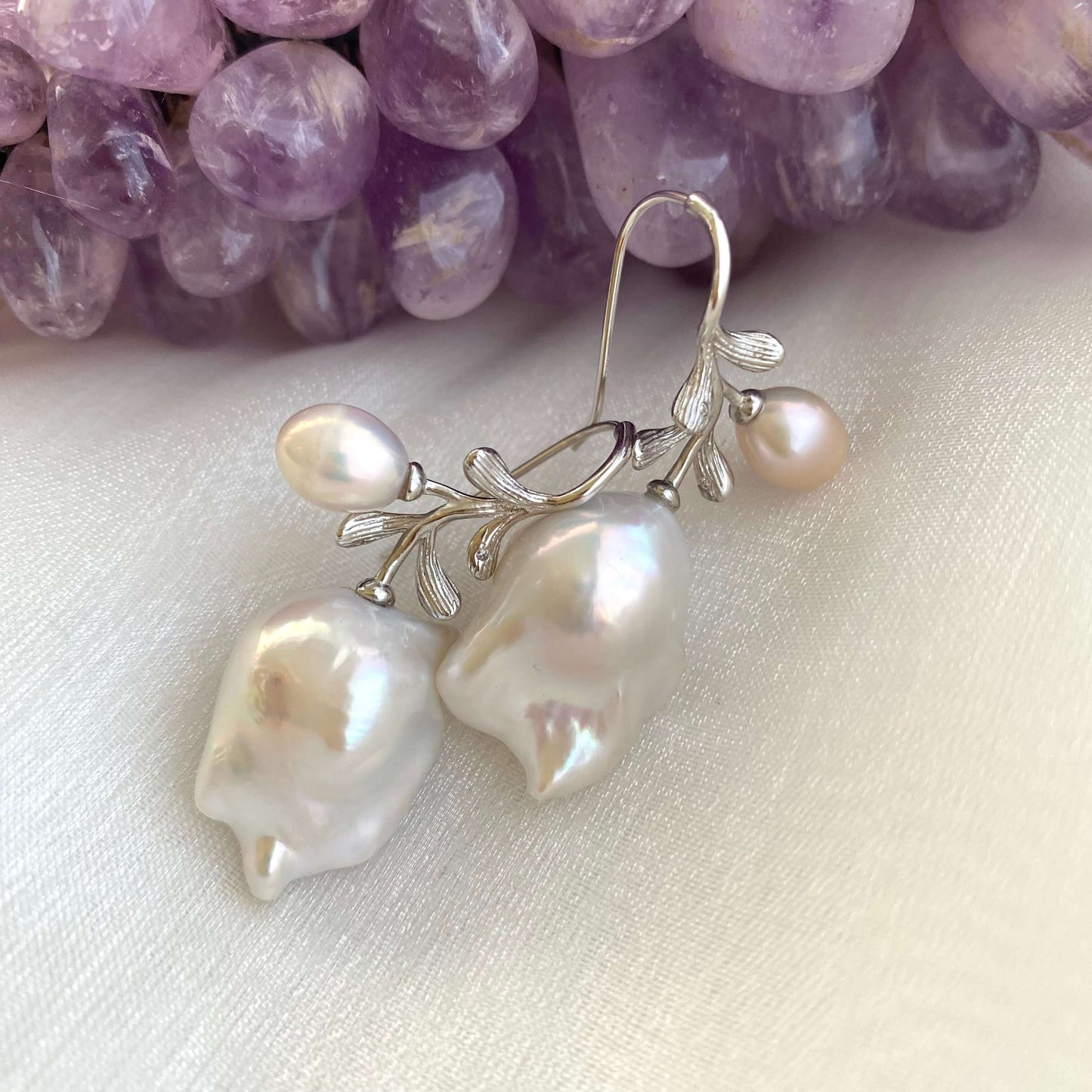 Handmade baroque pearl earrings in silver resting on white and amethyst background