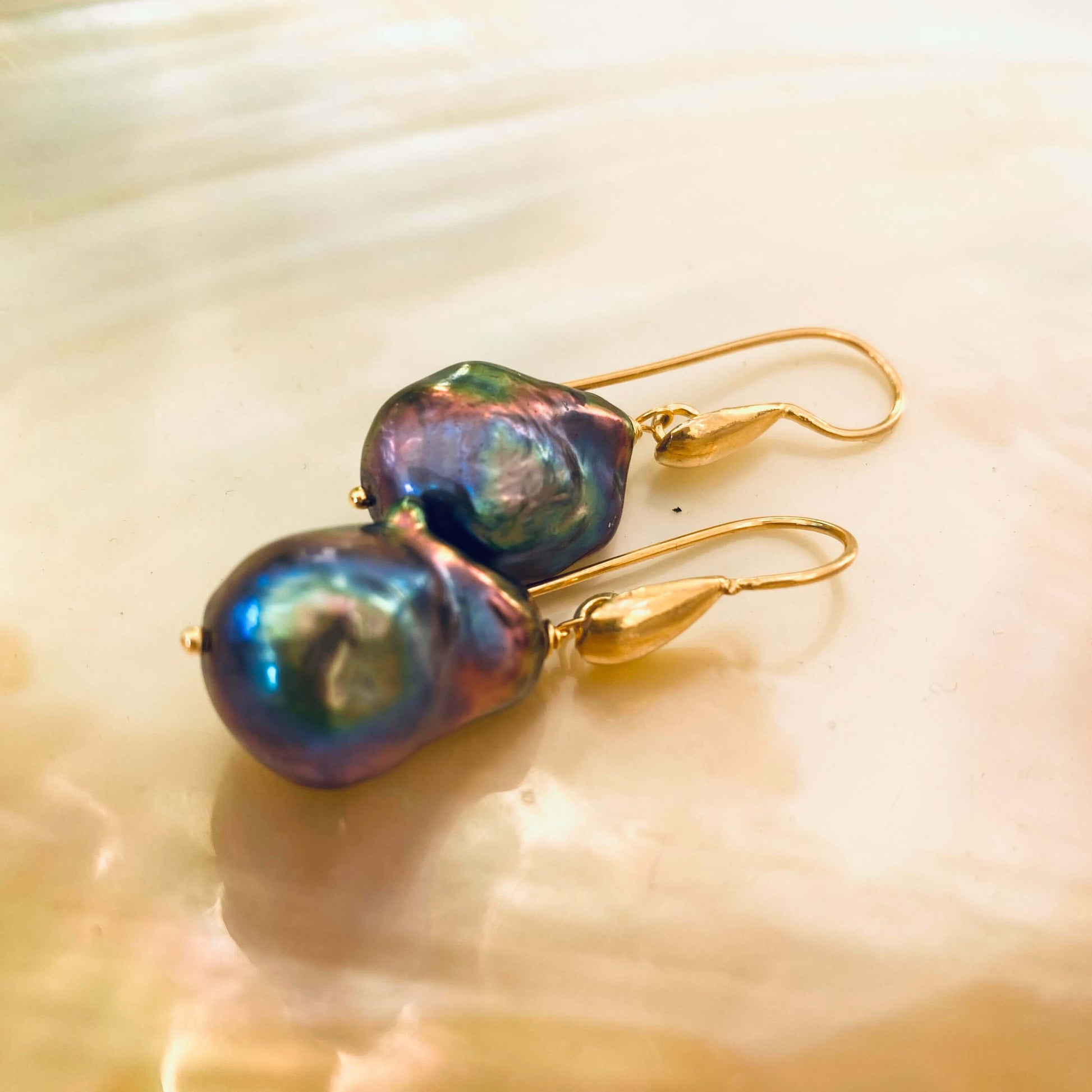 Handmade black baroque pearl drop earrings with gold vermeil hooks displayed on white pearl backdrop