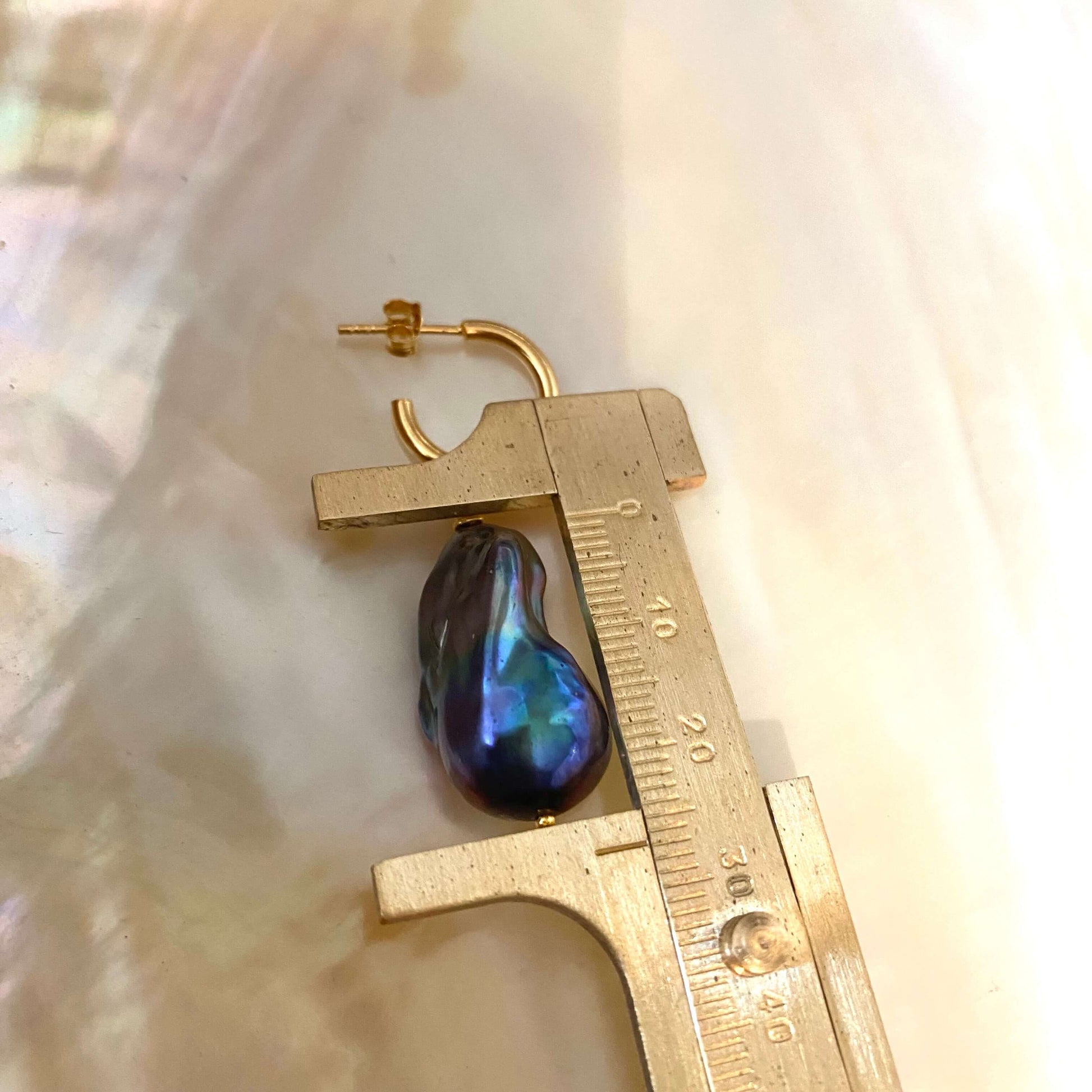 Black baroque pearl from hoop earrings measured by ruler for scale