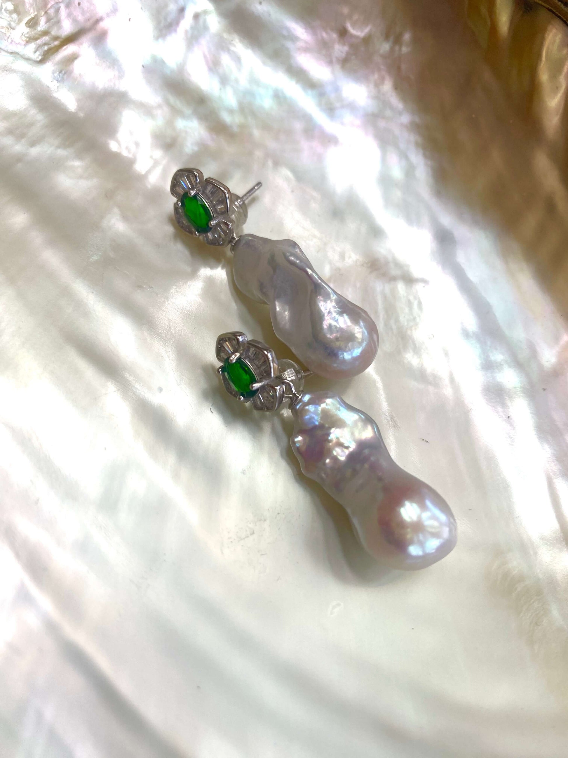 Detailed view of green diopside baroque pearl drop earrings — close-up of gemstone studs and pearls on white pearl shell background