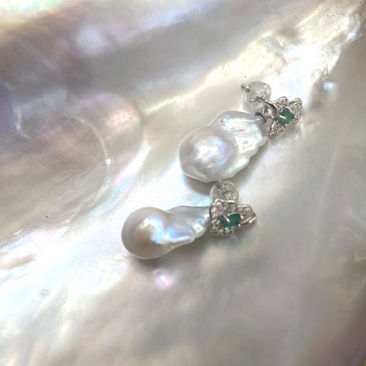 Emerald stud earrings with removable pearl drops on white pearl shell backdrop