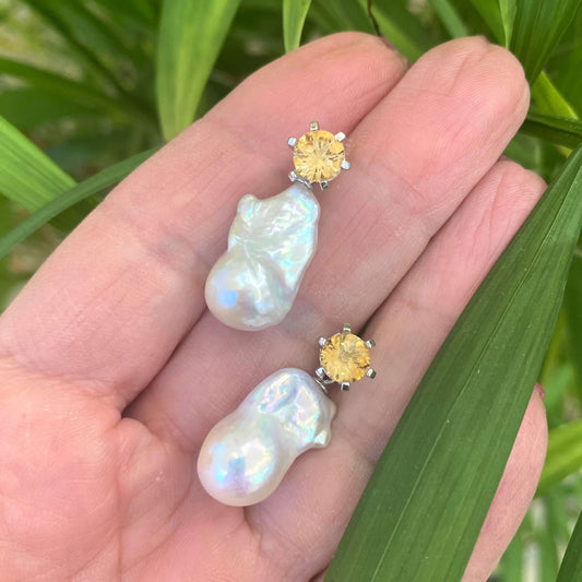 Citrine stud earrings with pearl drops held in hand against green leaf background