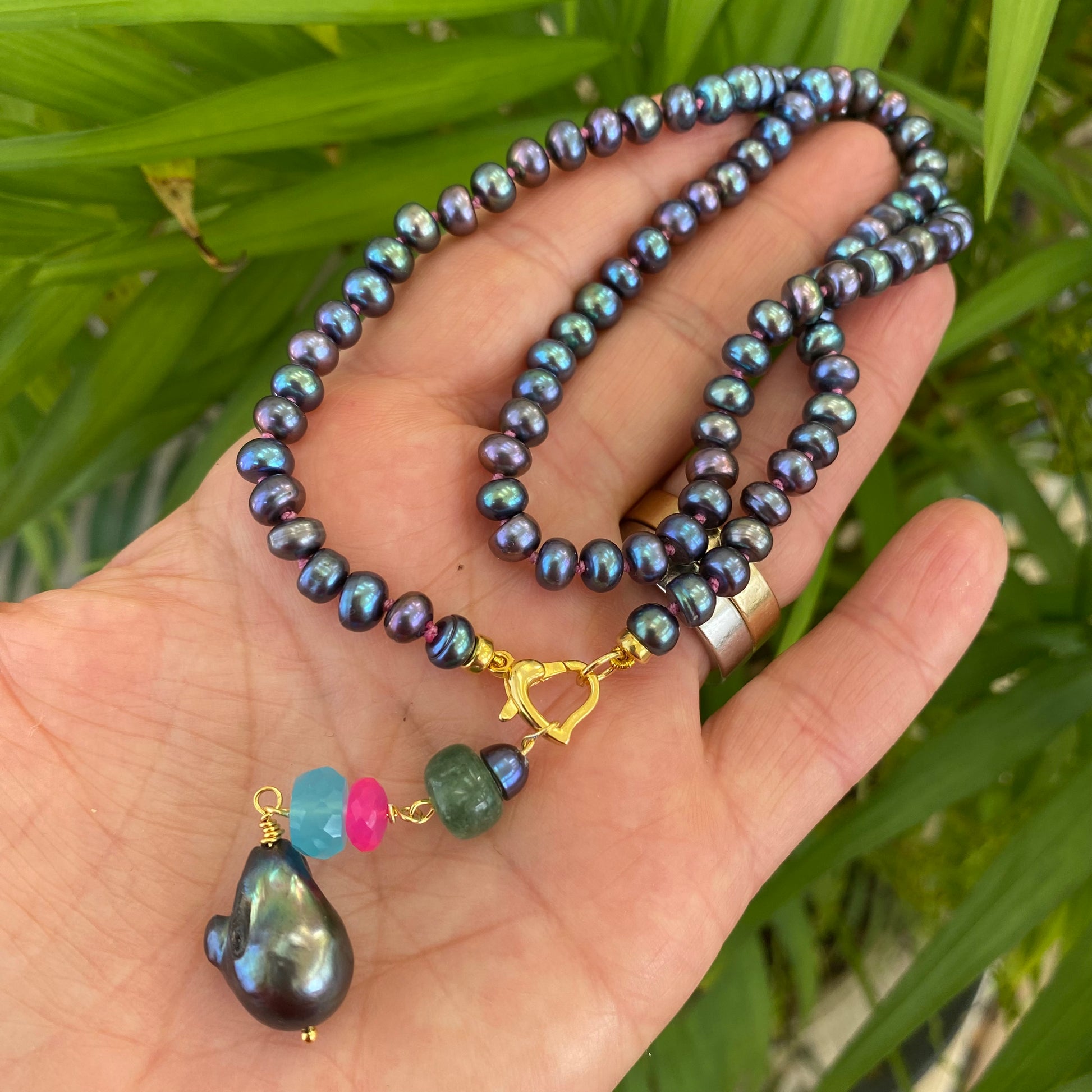 Black pearl necklace with chalcedony and chrysoprase held in hand showing removable gemstone pendant