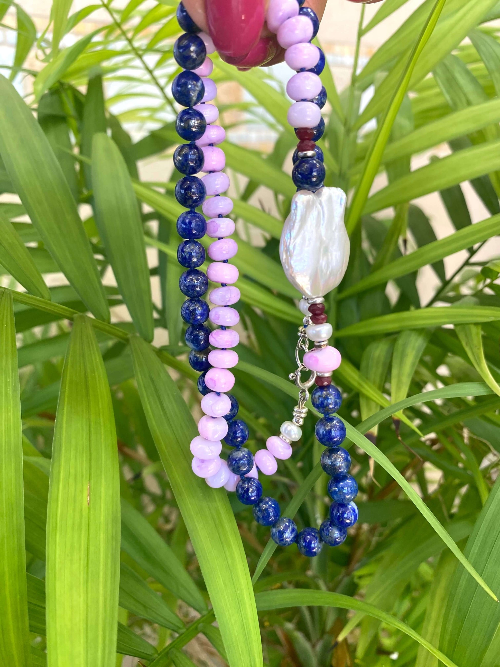 Lapis lazuli and baroque pearl necklace displayed against green leaf backdrop, handcrafted gemstone jewelry.