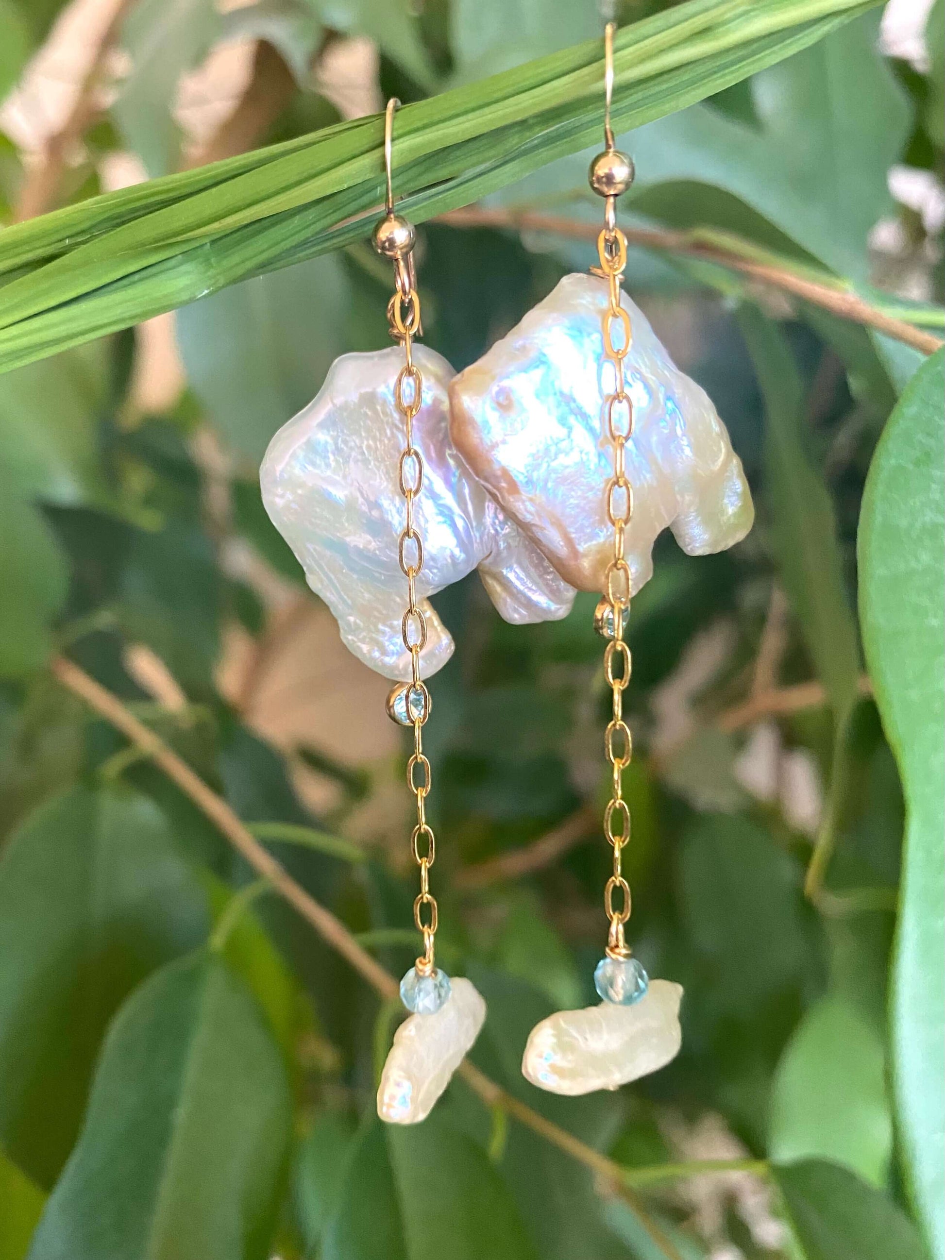 Close-up of boho pearl earrings gold filled photographed with green leaves — natural light jewelry shot showing blue topaz accent stones