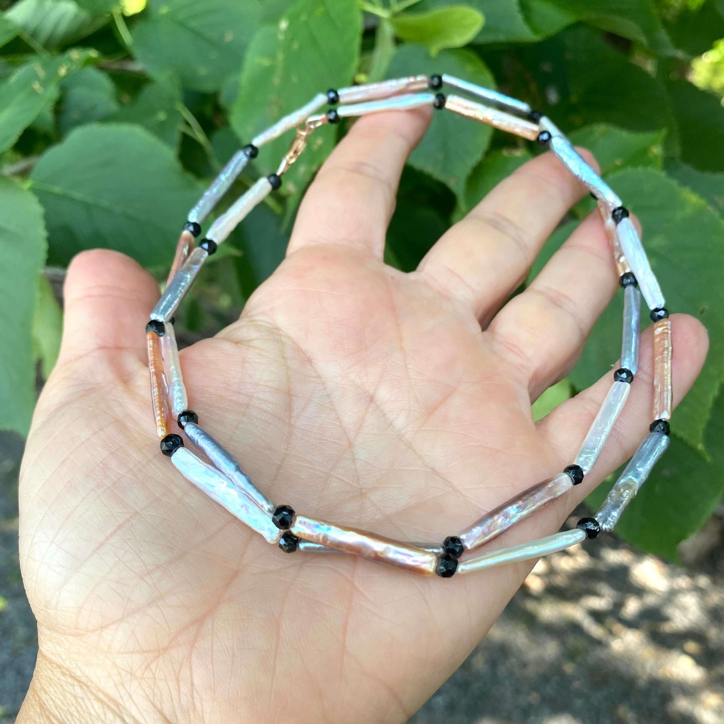 Pastel stick pearl necklace featuring stick pearls in pastel hues and black spinel accents, hand displayed against greenery.