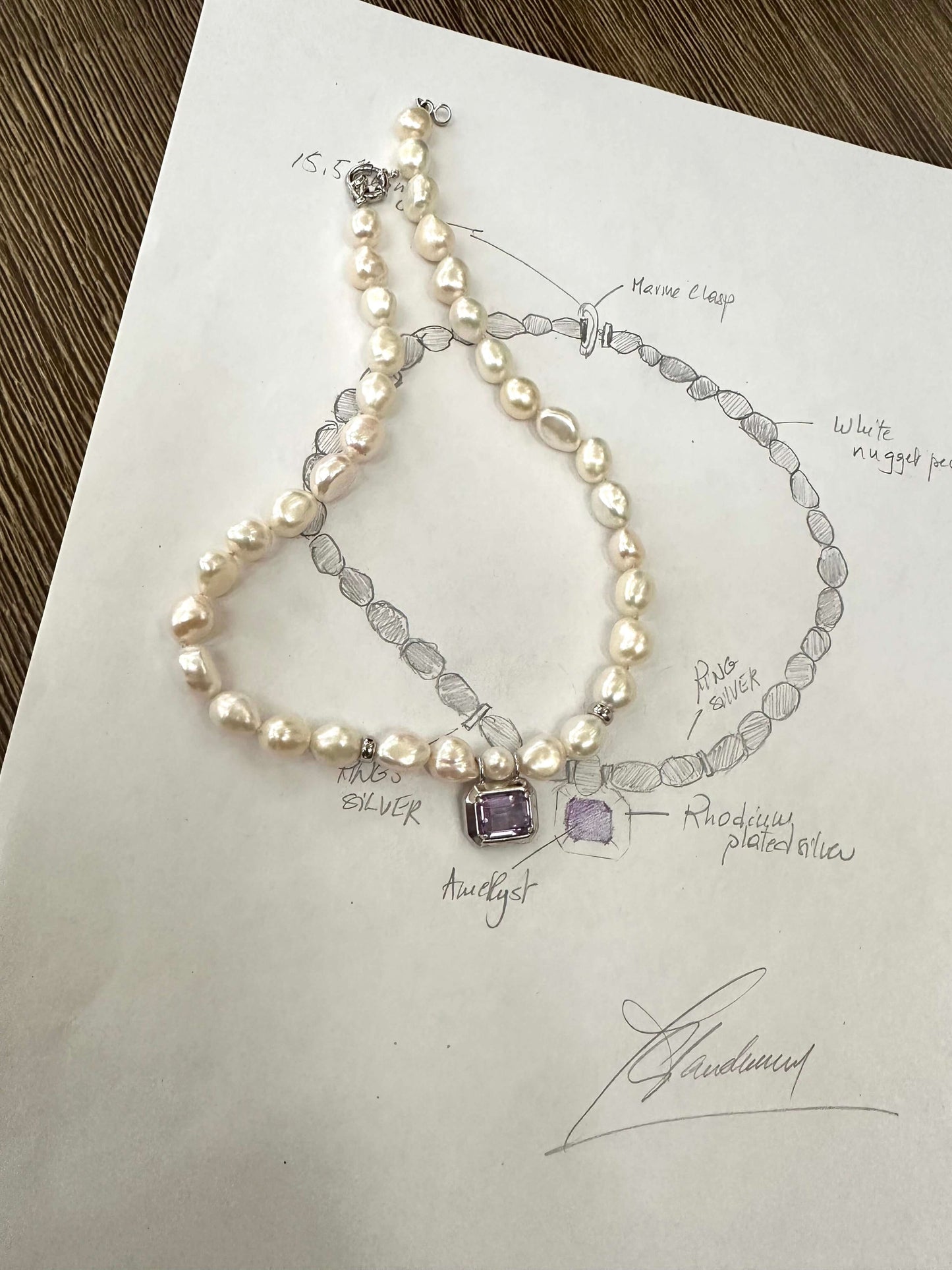 White nugget pearl necklace with amethyst pendant design sketch and necklace laid out on paper.