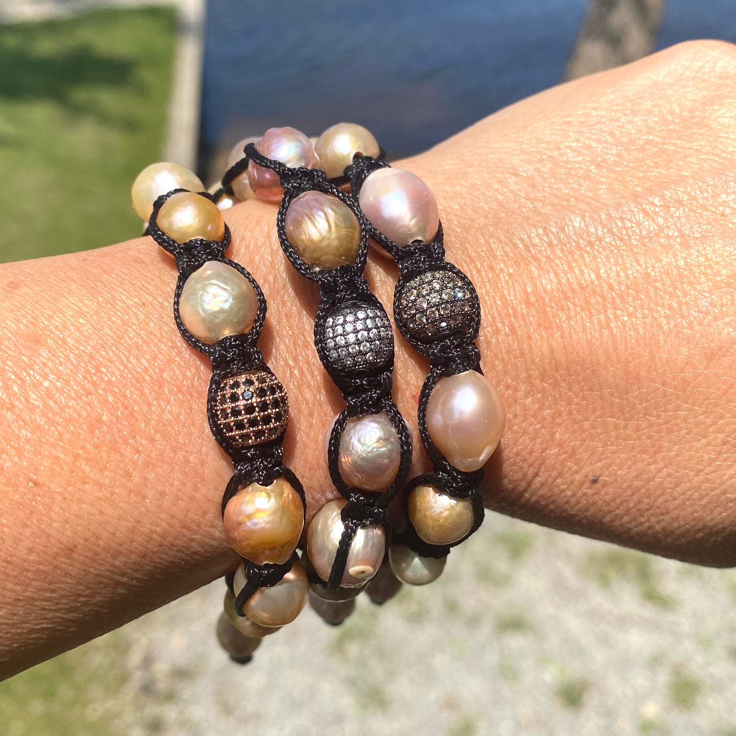 Baroque pearl bracelet featuring pastel pearls and black thread worn on wrist by the water.
