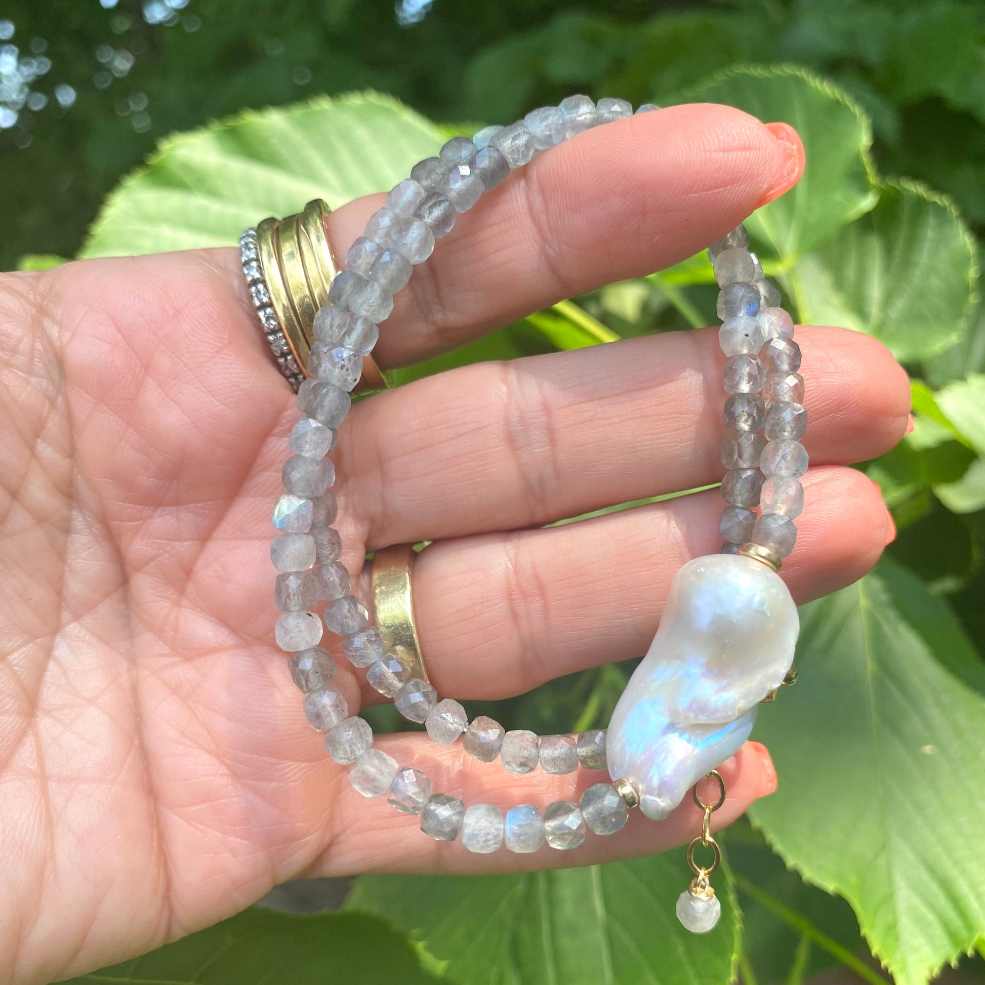 Labradorite necklace with blue flash and baroque pearl displayed in hand, showcasing delicate craftsmanship and elegance.