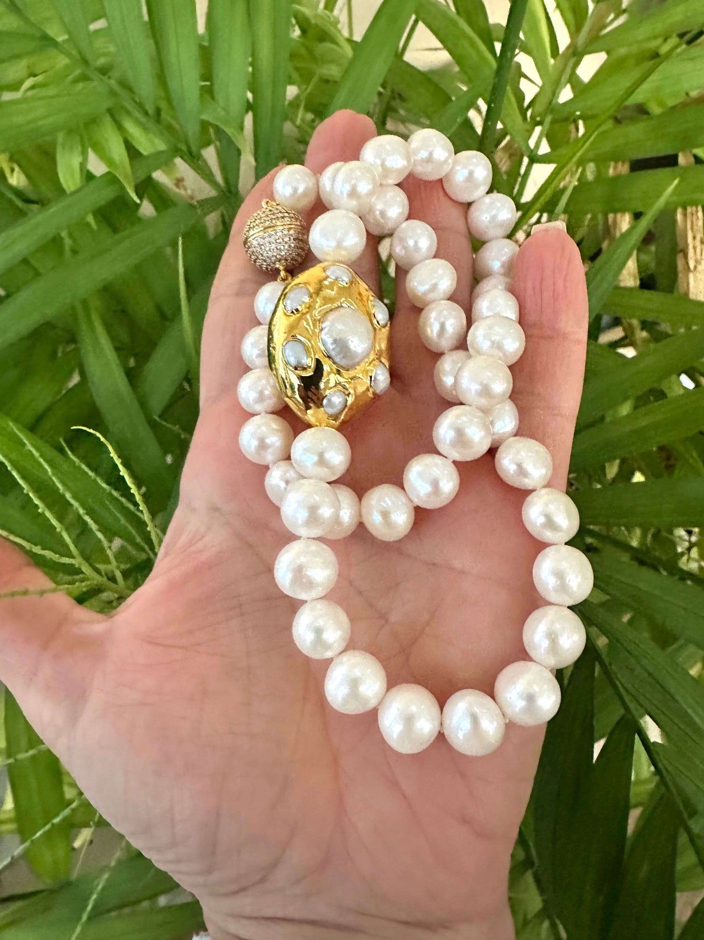 White potato pearl necklace showcased in a hand, featuring a gold focal accent among luminous freshwater pearls.