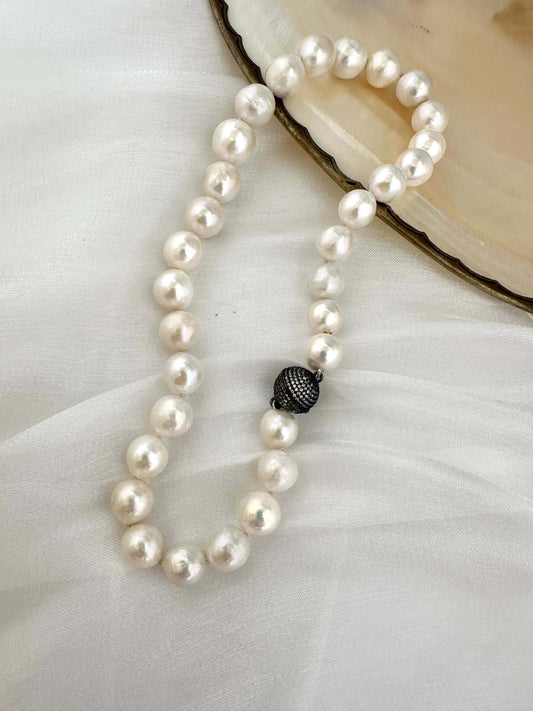 White Edison pearl necklace with large pearls and gunmetal pavé magnetic clasp, elegantly displayed on soft fabric.
