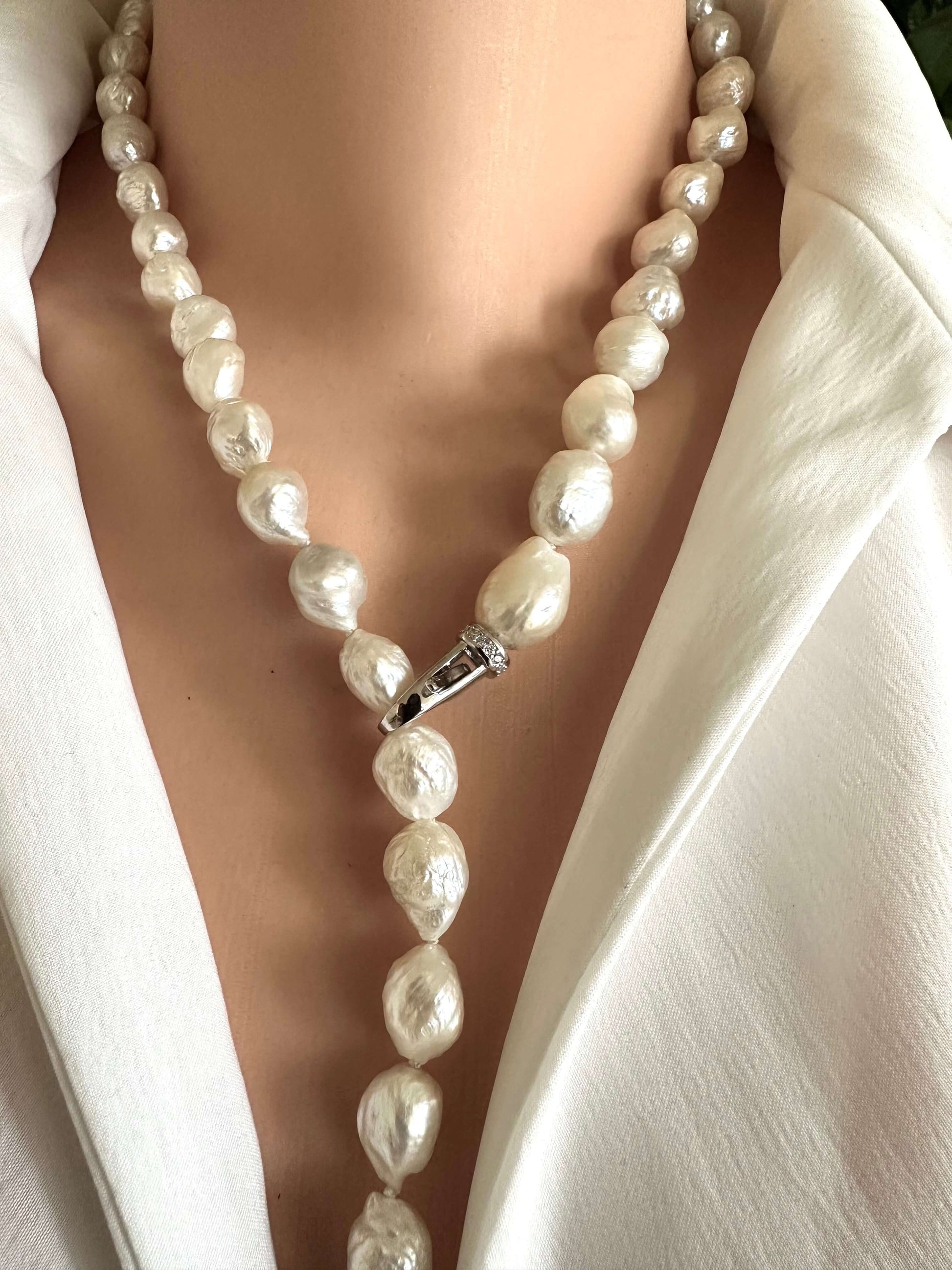 Edison baroque pearl Y necklace featuring hand knotted pearls and a rhodium clasp worn on a white blouse.