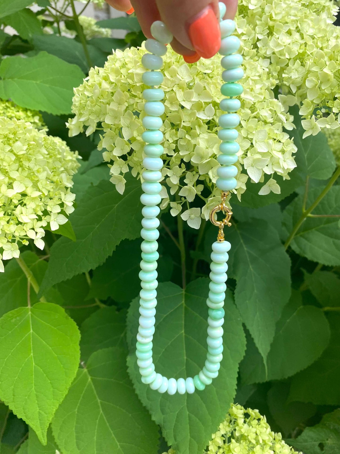 Green opal candy necklace displayed among lush green foliage and beautiful flowers.