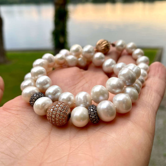 Rose gold pearl necklace held in hand at sunset by a river, showing luminous pearl lustre.