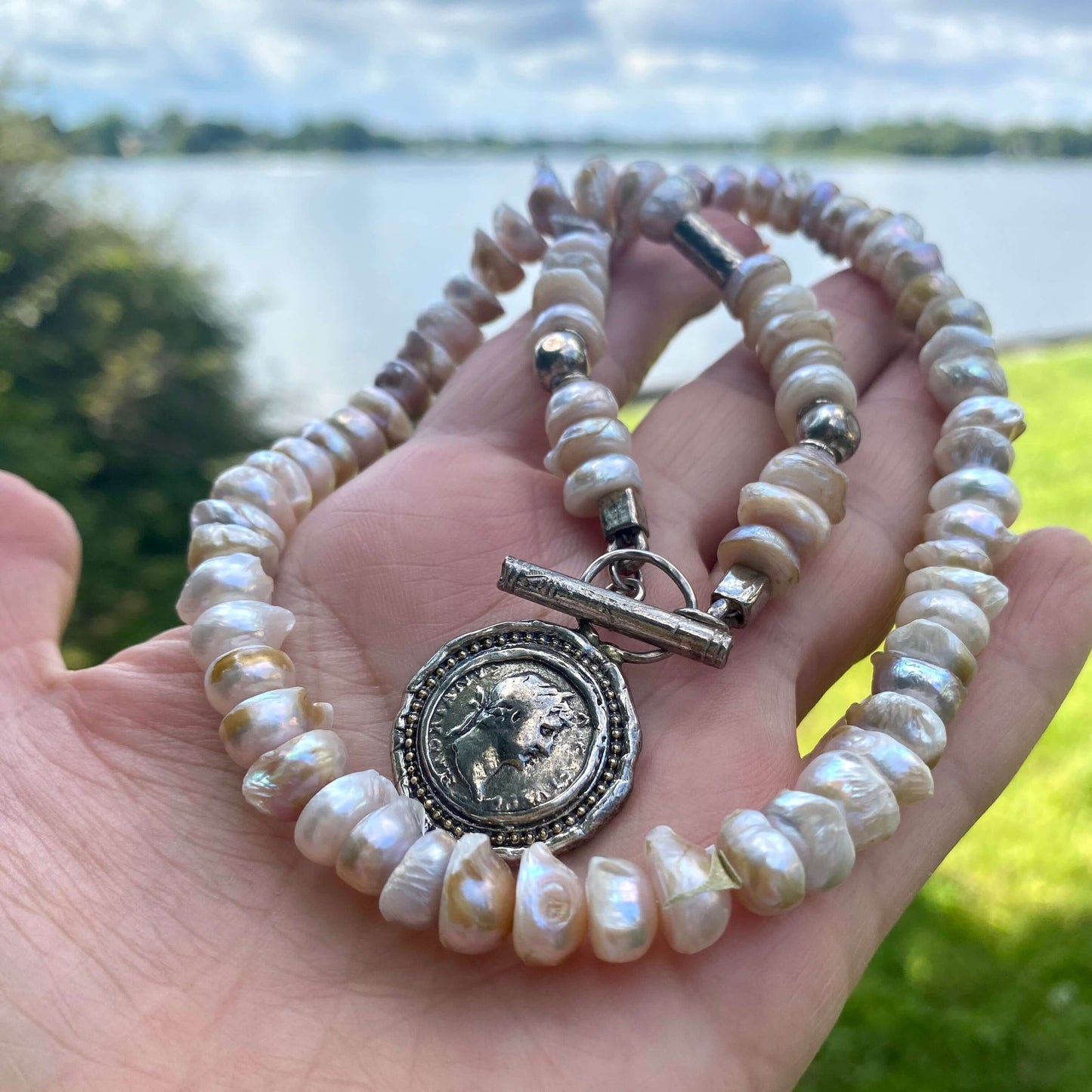 Lavender Baroque Pearl Necklace – Silver Roman Coin Toggle Clasp showcasing unique lavender pearls by a lakeside.
