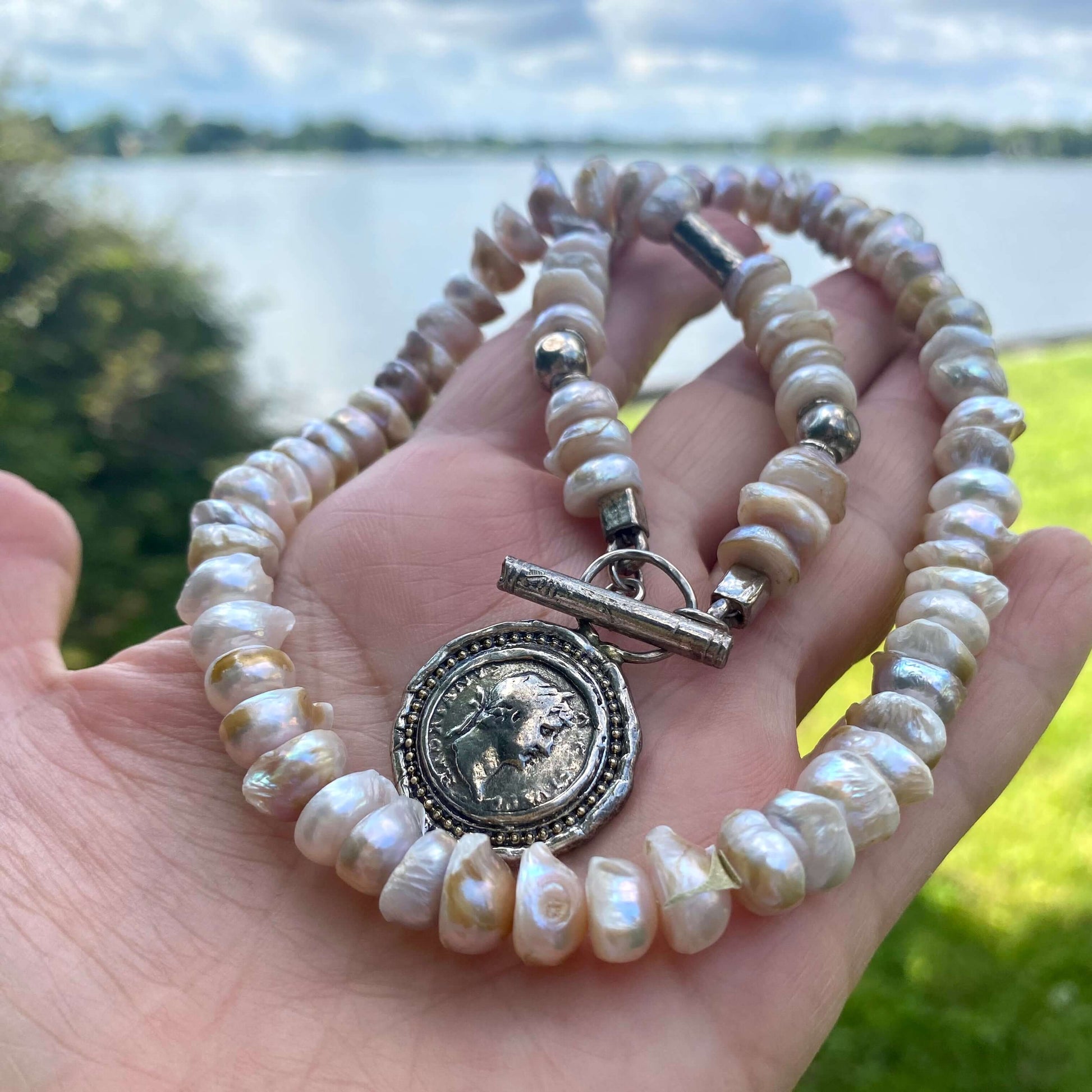 Lavender Baroque Pearl Necklace – Silver Roman Coin Toggle Clasp showcasing unique lavender pearls by a lakeside.