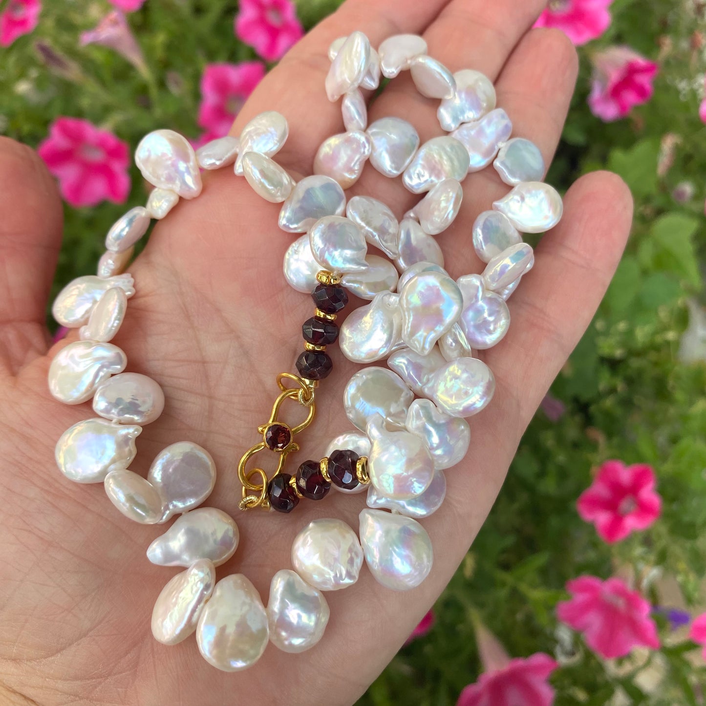 Keshi pearl necklace featuring lustrous keshi pearls and garnet beads in a hand against a floral backdrop.
