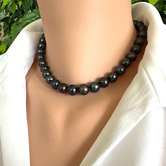 Black beaded necklace on a person wearing a white shirt with a blurred green background