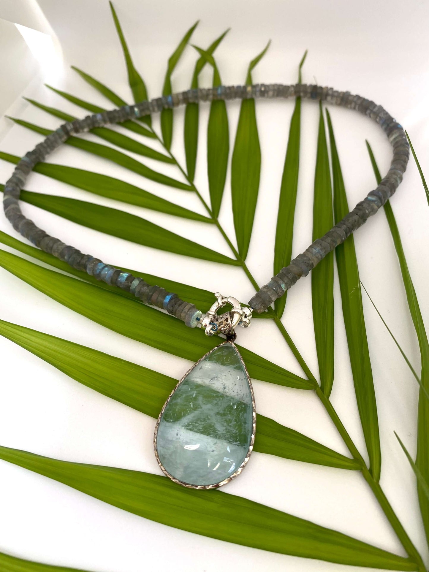 Aquamarine teardrop pendant in oxidized sterling silver on a leaf background, showcasing its watery blue tones.