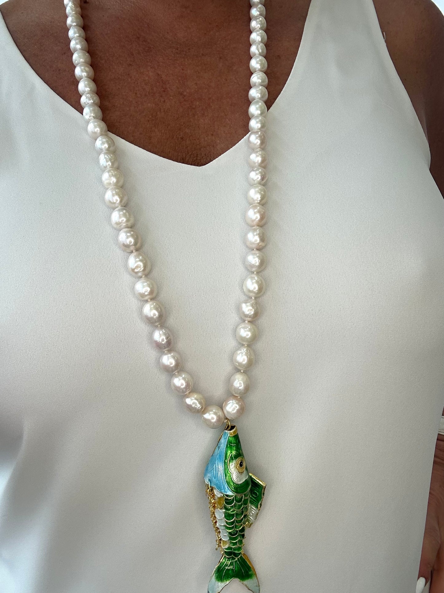 Pearl necklace with a fish pendant worn by a person in a white top.