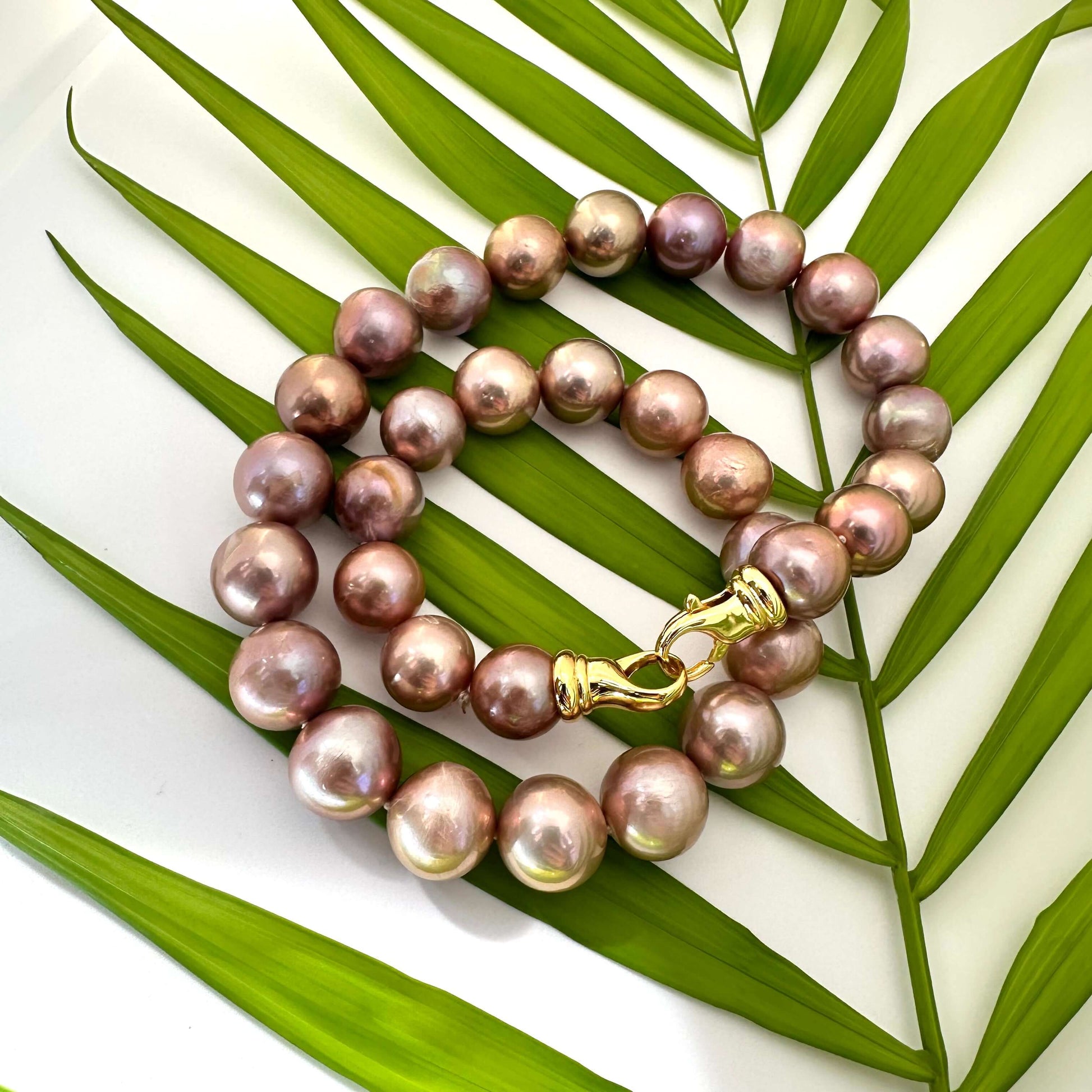 Metallic Edison Pearl Necklace showcasing 12–14mm pearls, handcrafted design, set against green palm leaves.