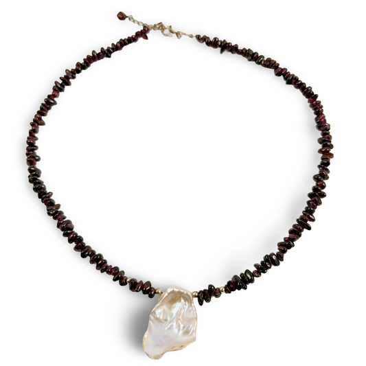 A beaded necklace featuring dark red polished stone chips with a large, irregular white baroque pearl pendant, displayed on a clean white background.