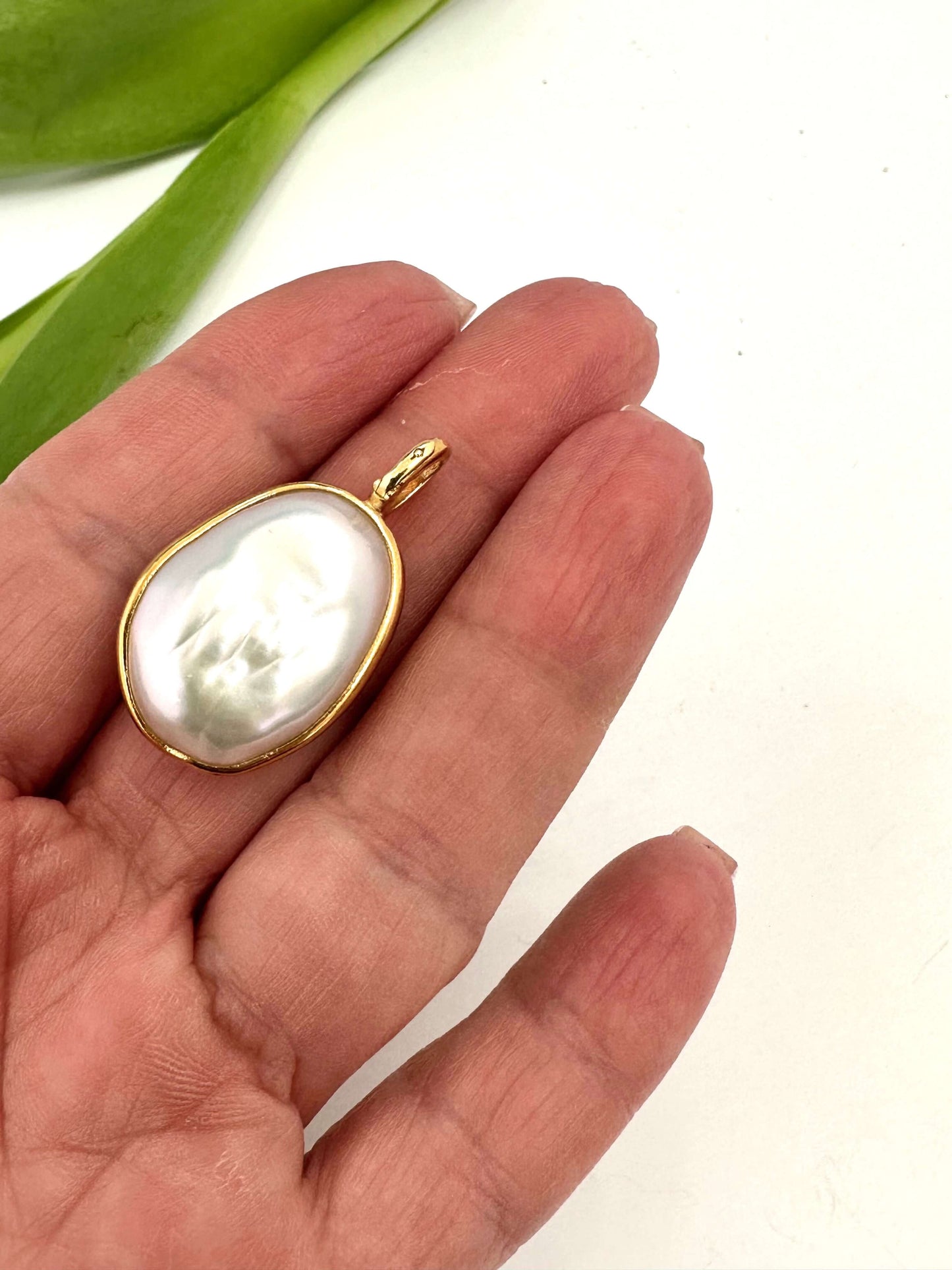 Baroque pearl pendant in gold vermeil held in a hand, showcasing its unique shape and soft iridescence.