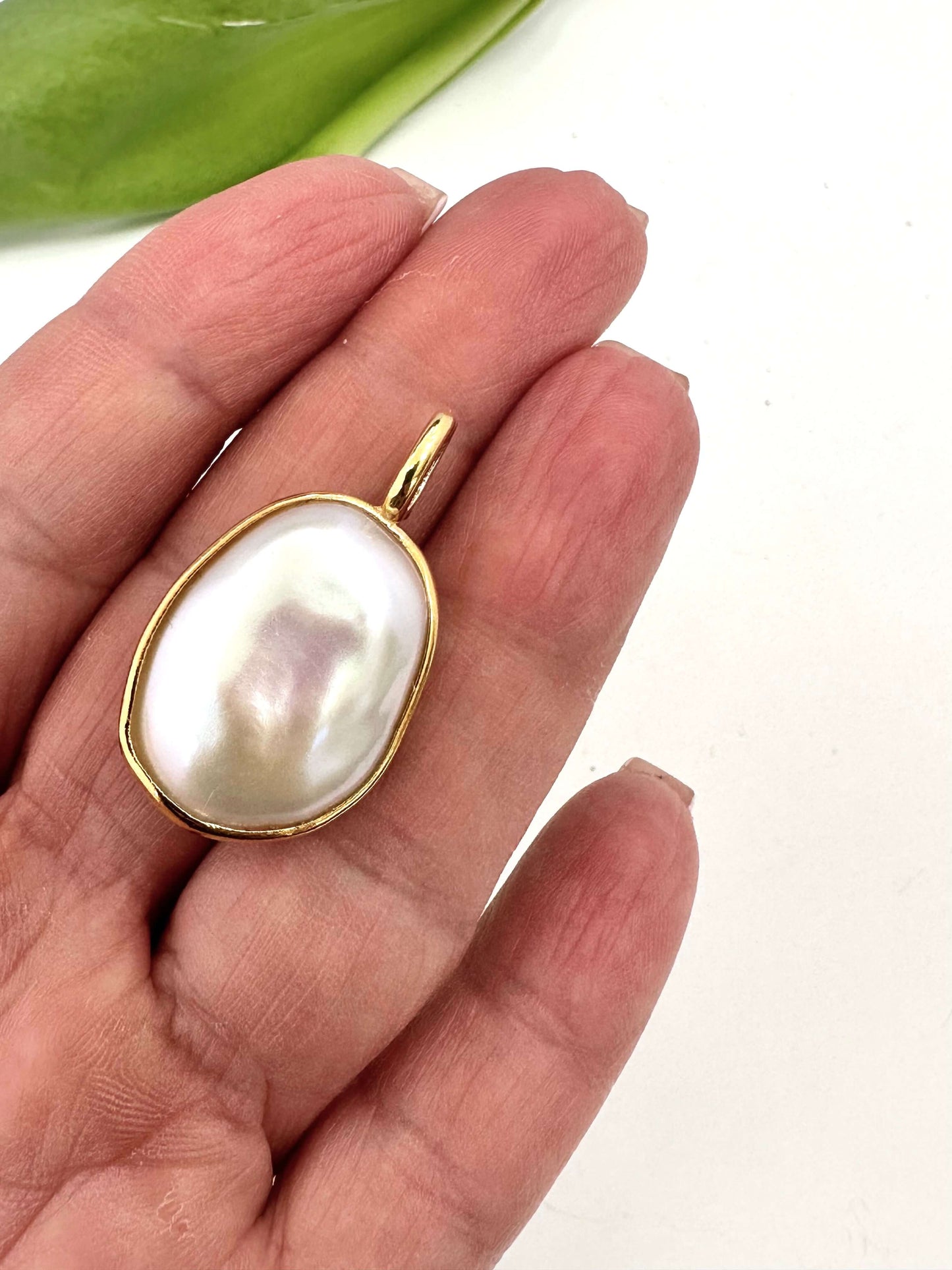 Baroque pearl pendant in gold vermeil held in a hand, showcasing its unique shape and iridescent surface.