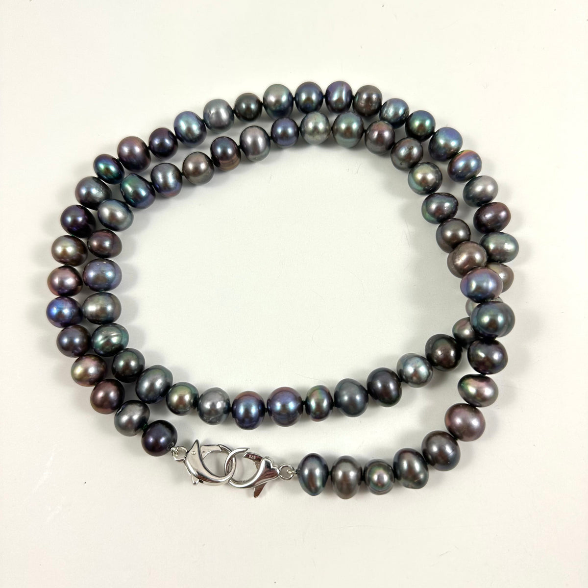 A necklace of dark, iridescent freshwater pearls with a silver lobster clasp, displayed on a plain off-white background.