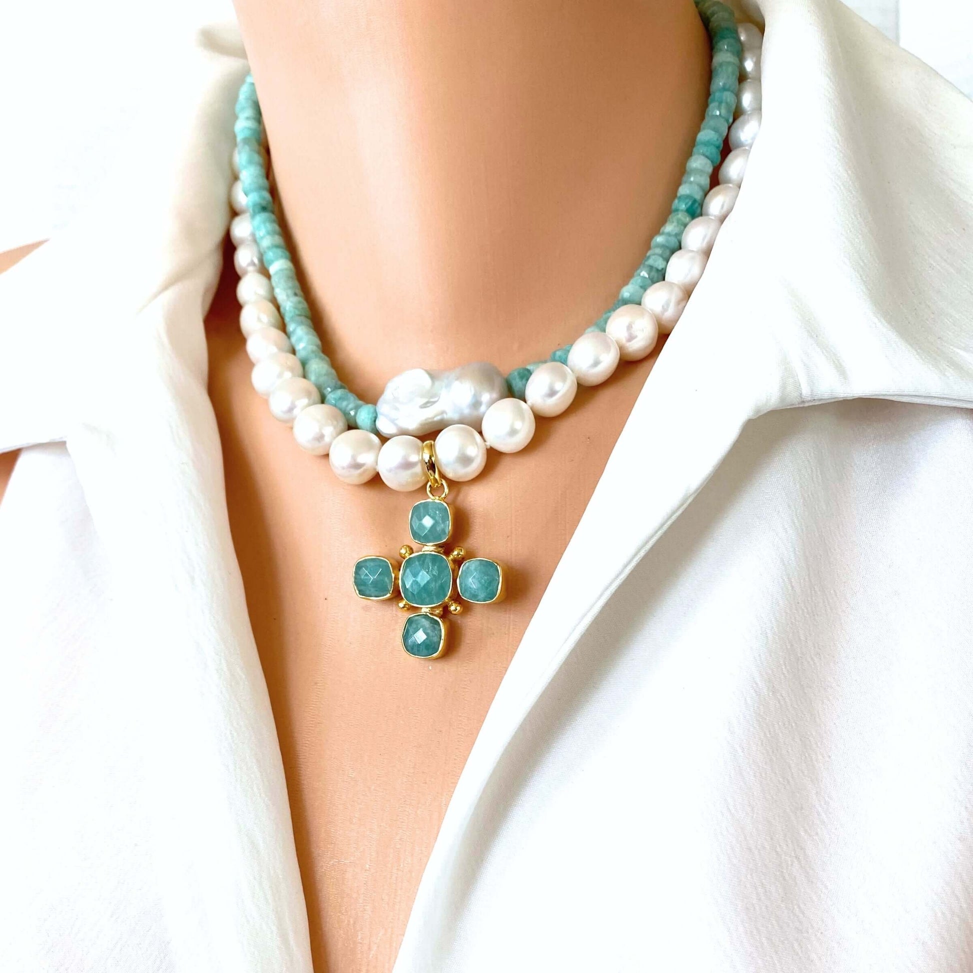 A close-up of a model wearing a double-strand necklace with white pearls, turquoise-blue beads, and a gold cross pendant with turquoise stones, styled with a white collared shirt.