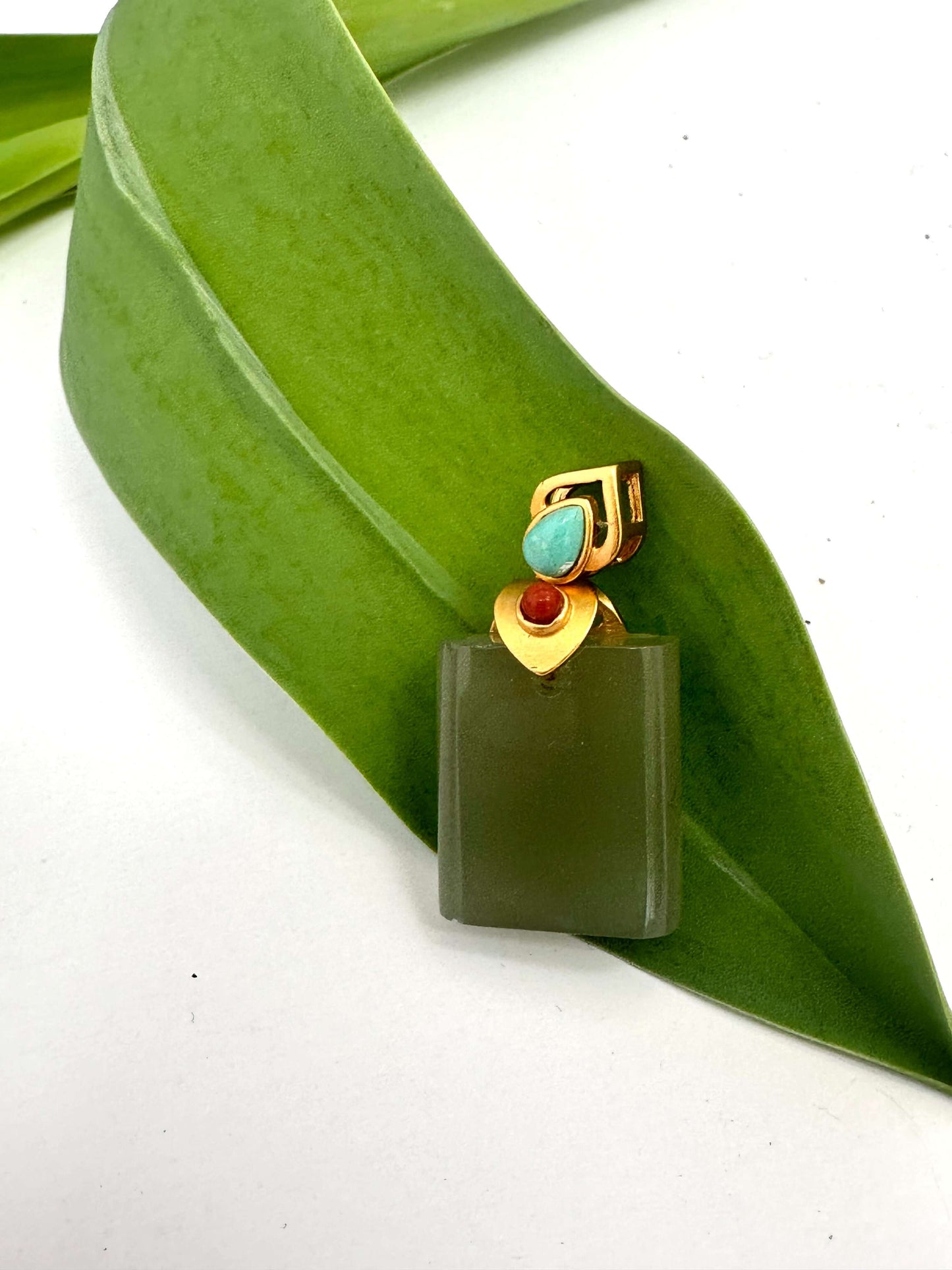 Hotan jade pendant with turquoise and red agate in gold vermeil on a green leaf.