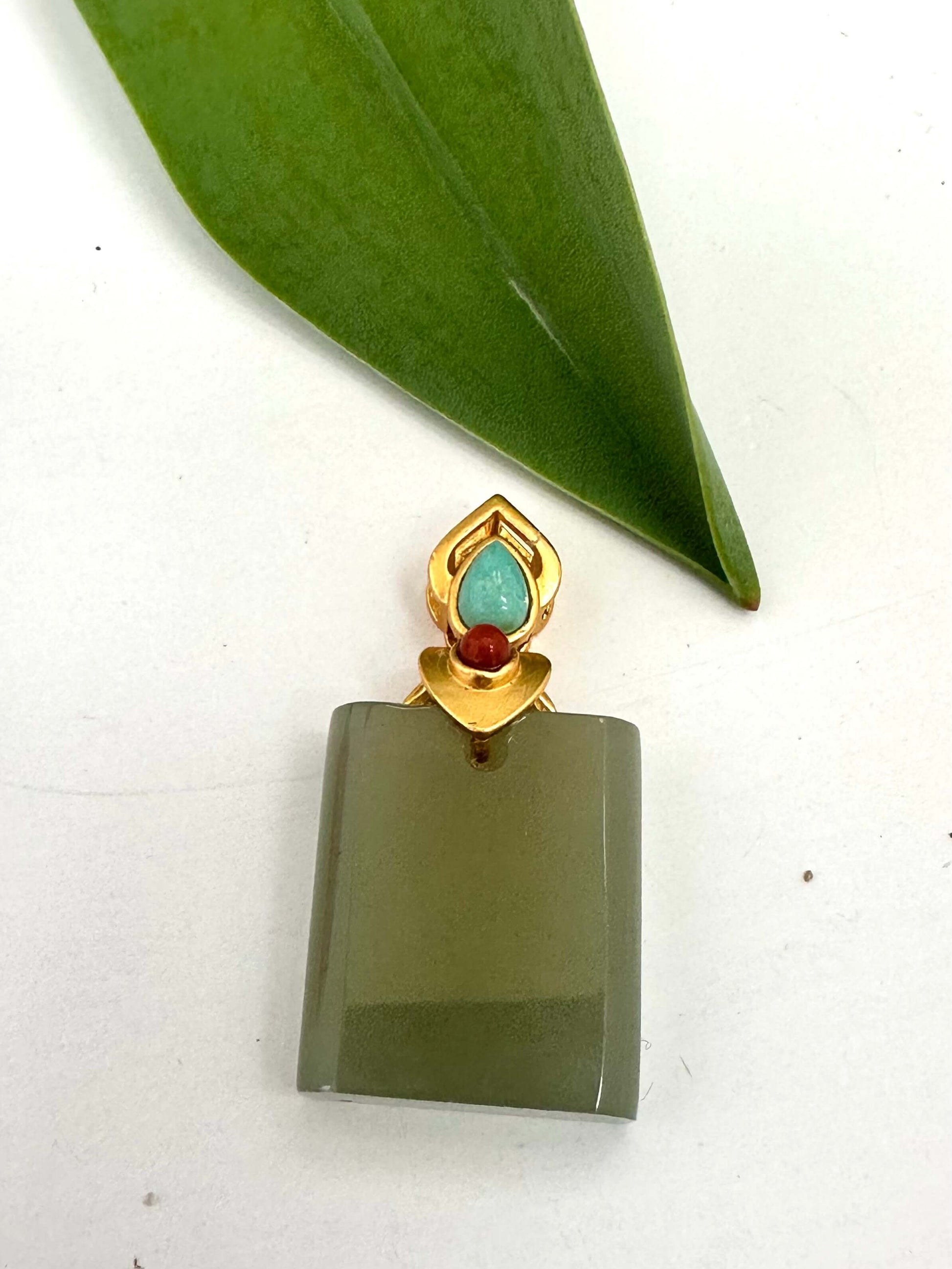 Hotan jade pendant with turquoise and red agate in gold vermeil on a plain background.