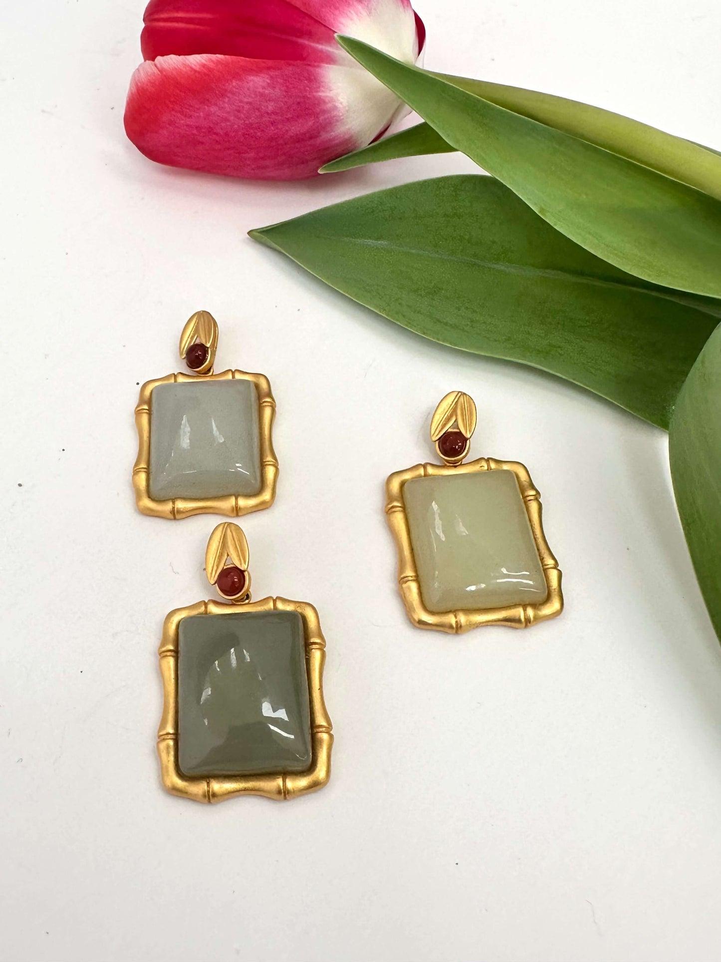 Bamboo style jade pendant with red agate displayed among green leaves and tulip flowers.