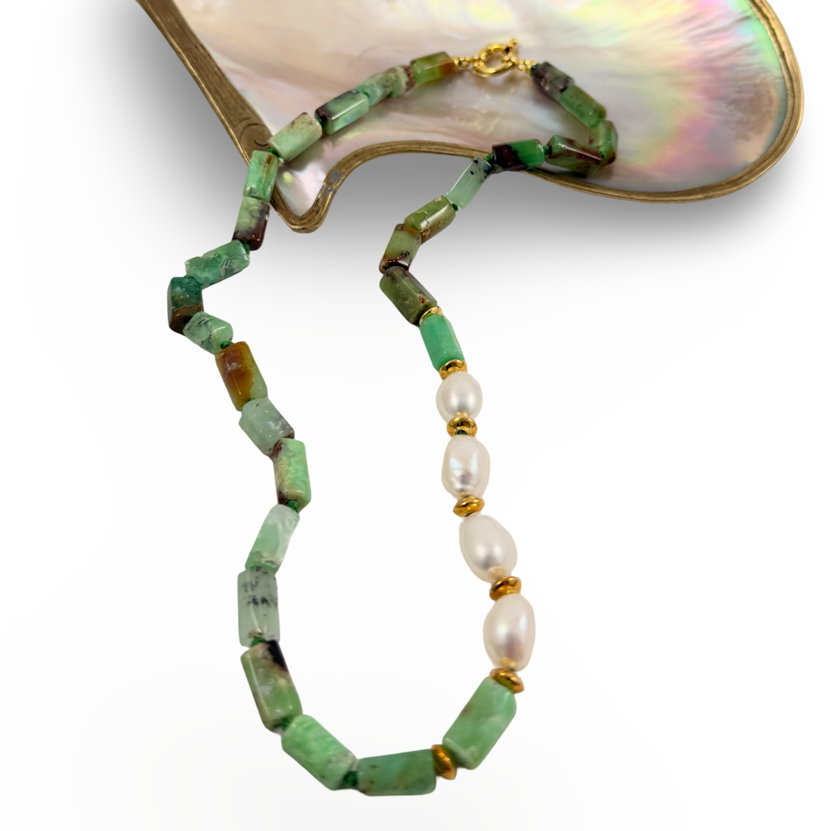 A beaded necklace with rectangular green stone beads, white pearl-like beads separated by small gold spacer beads, and a gold clasp, displayed against a white background with a mother-of-pearl shell prop.