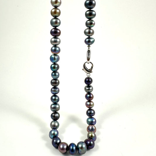 A strand of iridescent baroque pearls in shades of dark gray, blue, and purple, arranged in a U-shape with a silver lobster clasp on a white background.