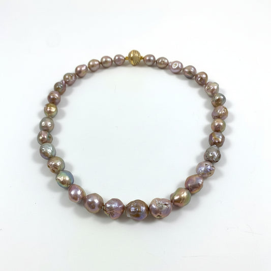 A beaded necklace made of irregular, lustrous baroque pearls in iridescent shades of bronze, purple, and green, with a small gold clasp, displayed on a plain white surface.