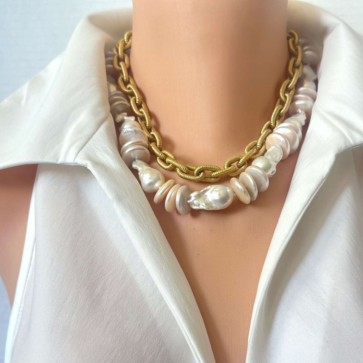 close up of gld chain and baroque pearl necklaces layered on a mannequin